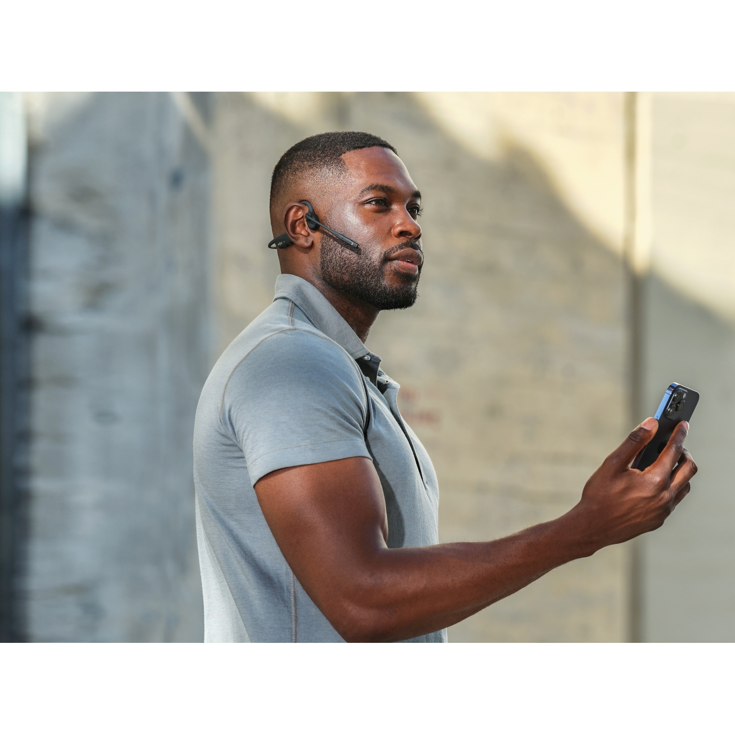 Een man met headset houdt een smartphone vast. Grijze achtergrond.