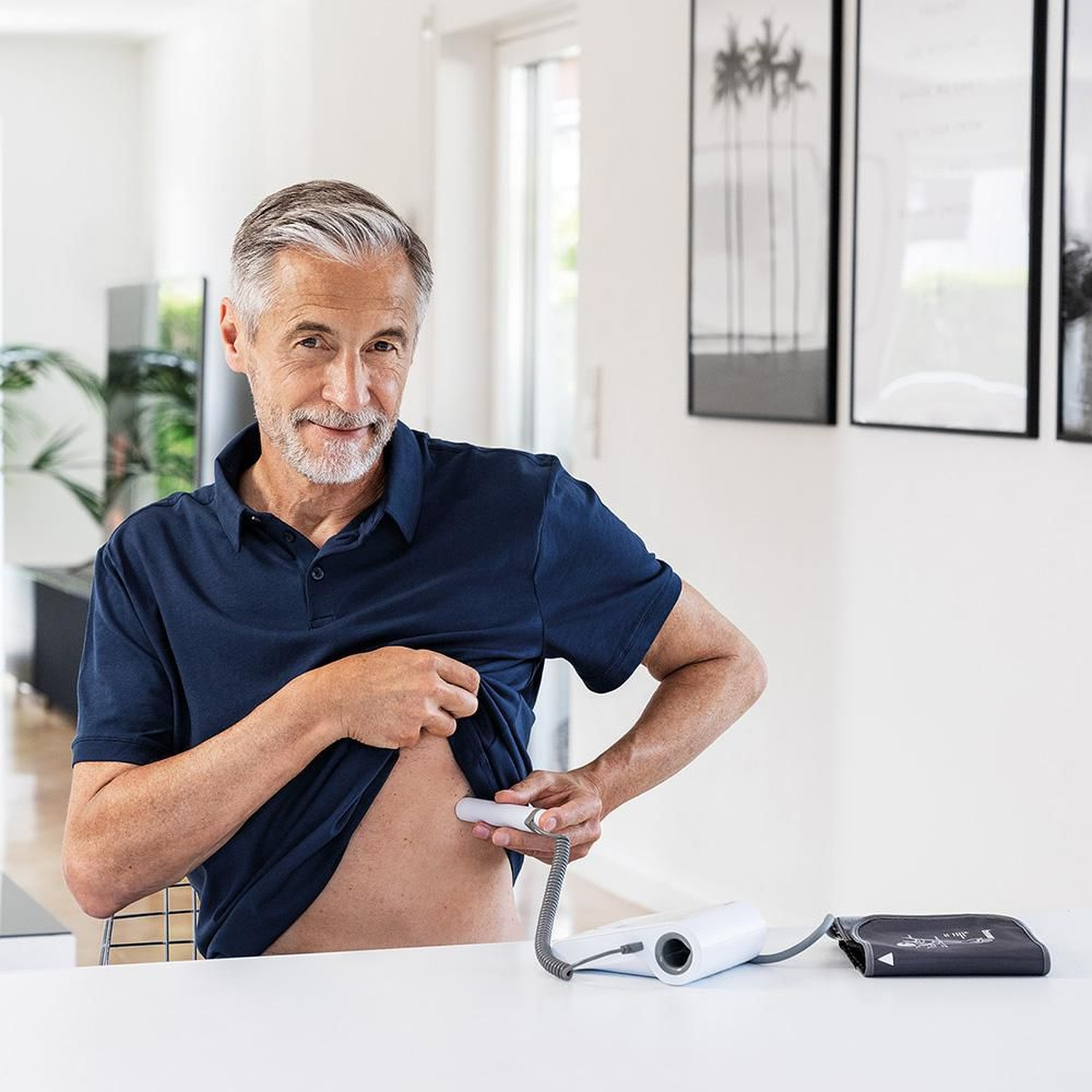 Un uomo anziano in polo blu solleva la maglietta per usare un dispositivo medico bianco sull'addome.