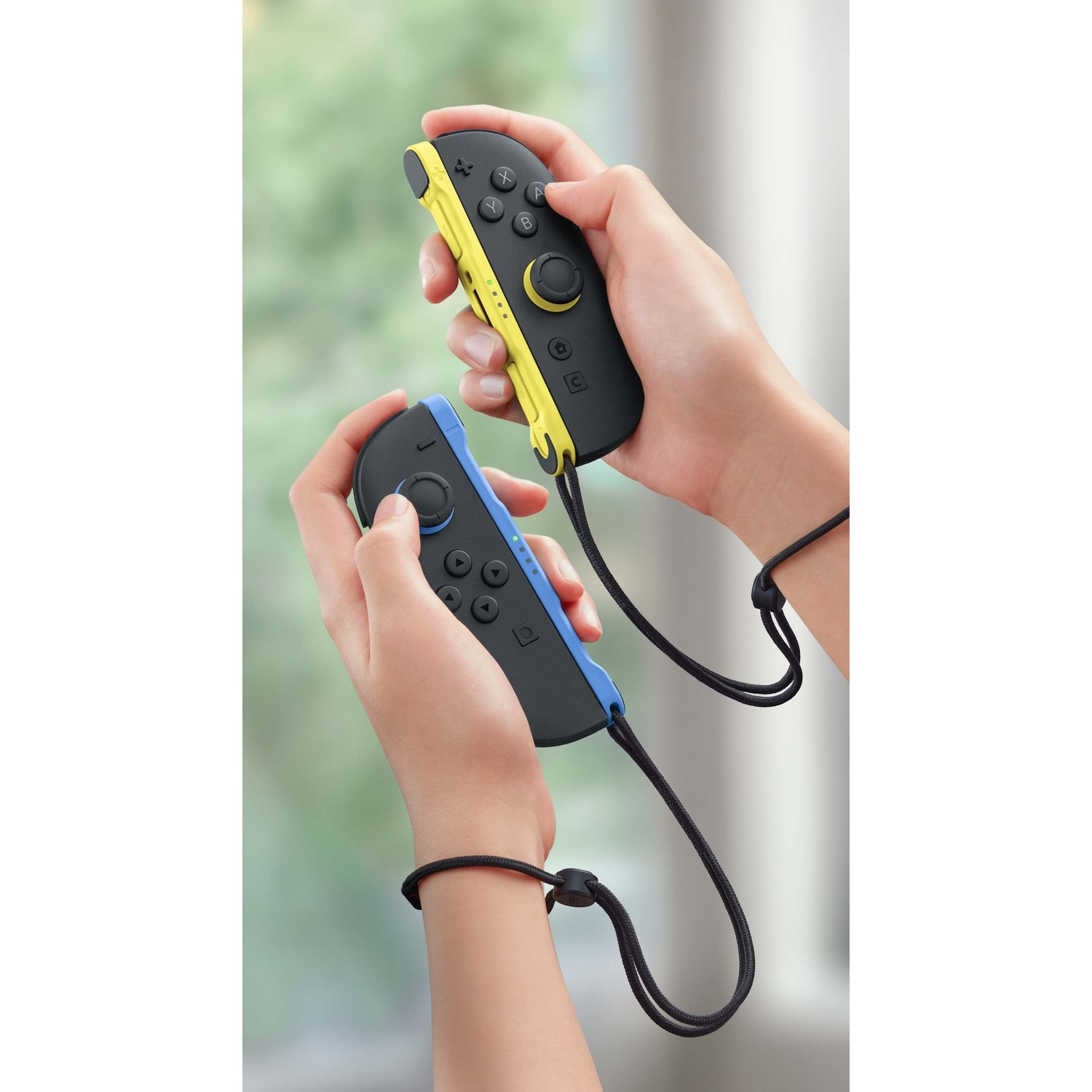 Due mani tengono controller Joy-Con Nintendo Switch gialli e blu.