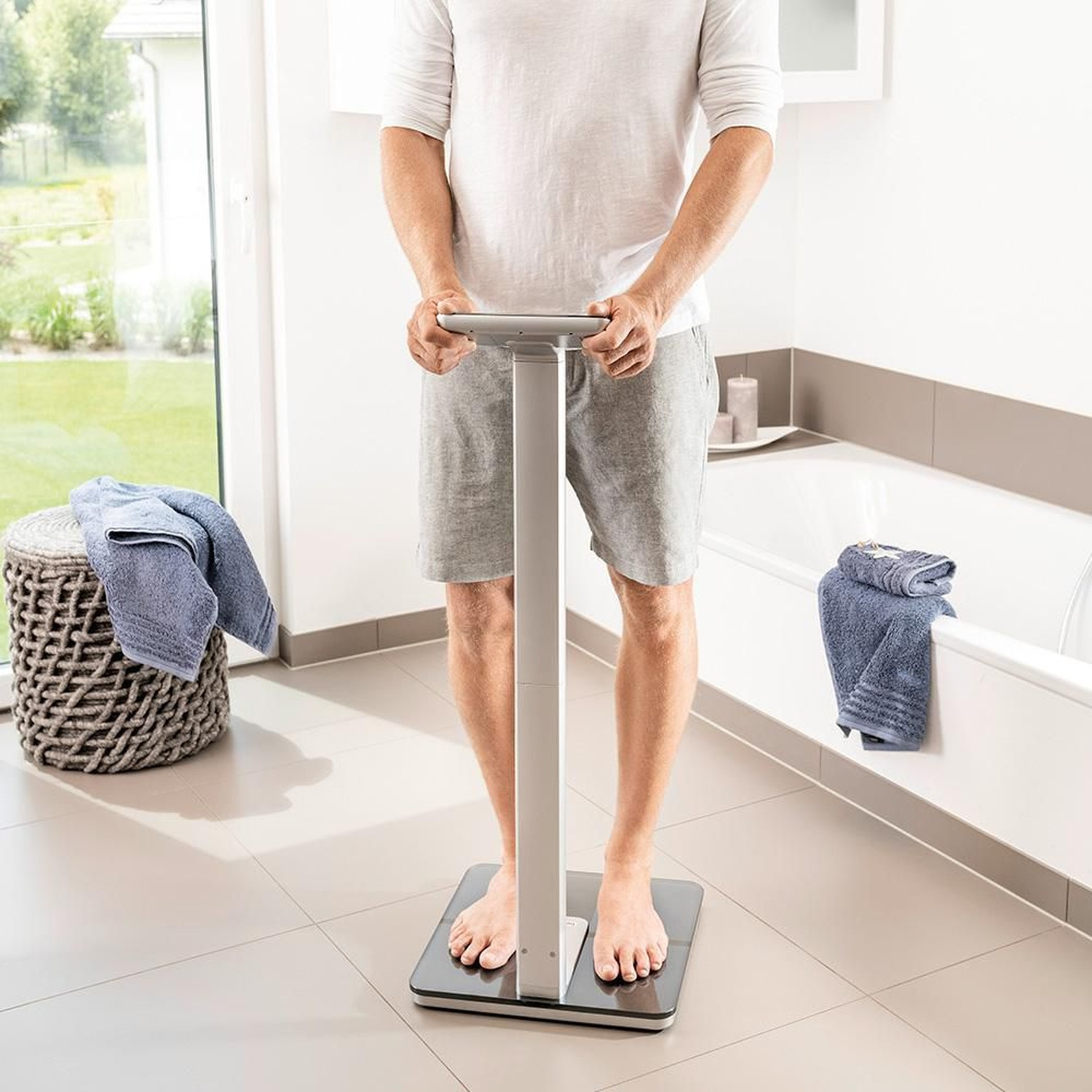Uomo su bilancia in bagno con asciugamani vicino a vasca e cesto.