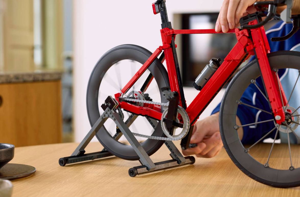 Ein rotes Lego-Rennrad auf einem Trainingsständer, das von Händen justiert wird.