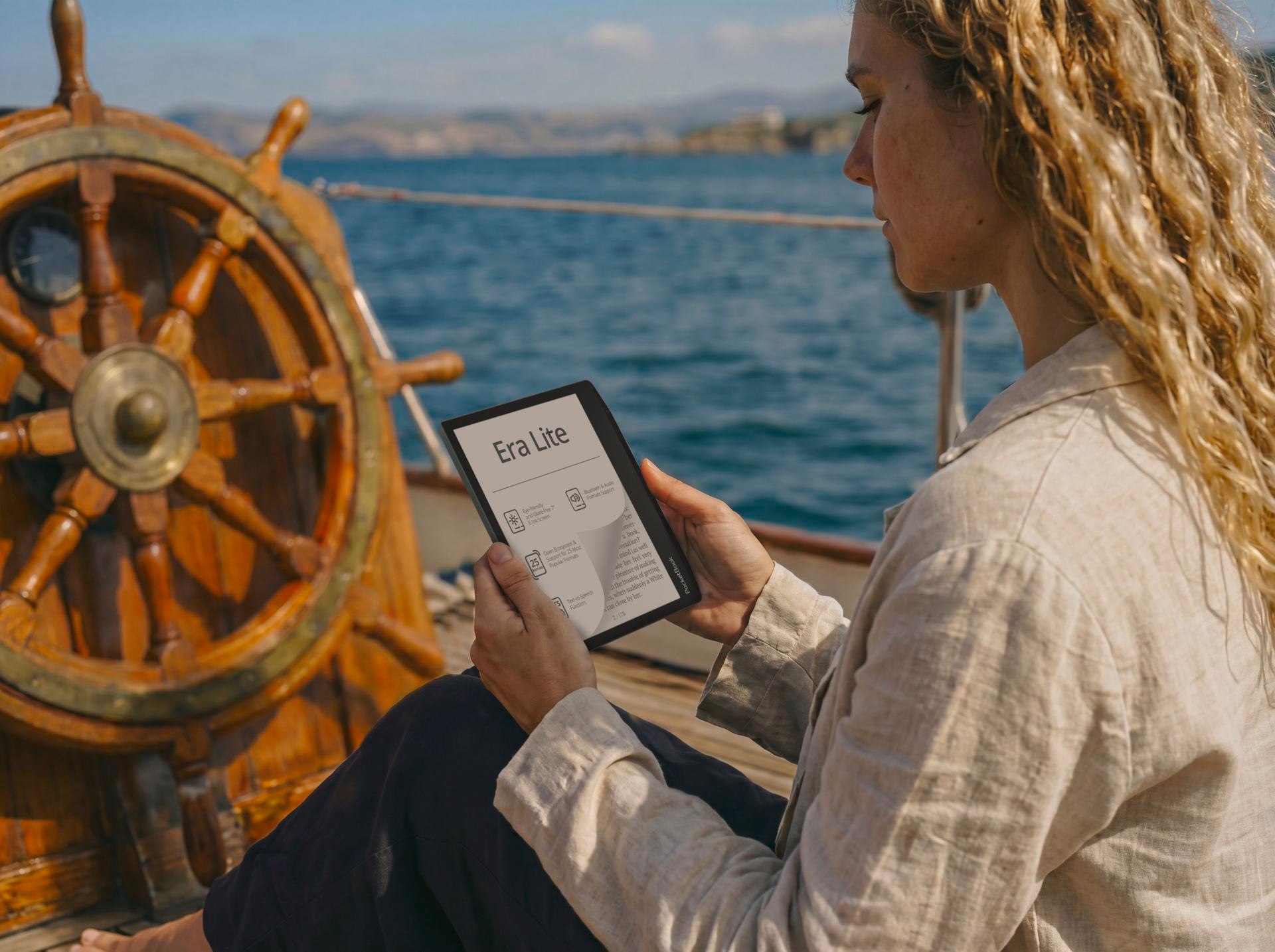 Frau auf einem Boot liest E-Reader am hölzernen Schiffsrad. Meer und Himmel im Hintergrund.