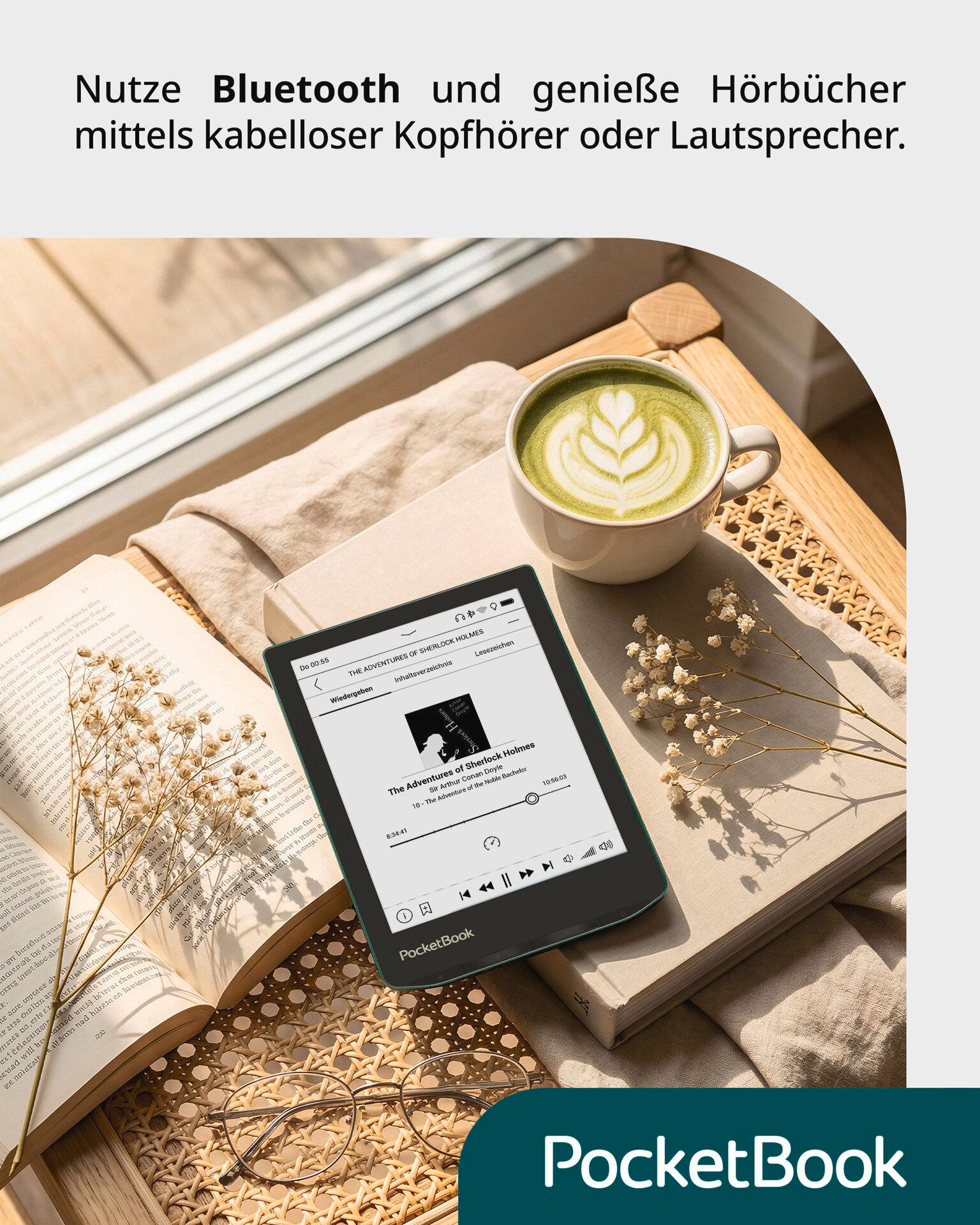 E-Reader mit Hörbuchwiedergabe, Kaffee, offenem Buch und Brille auf einem Tisch.