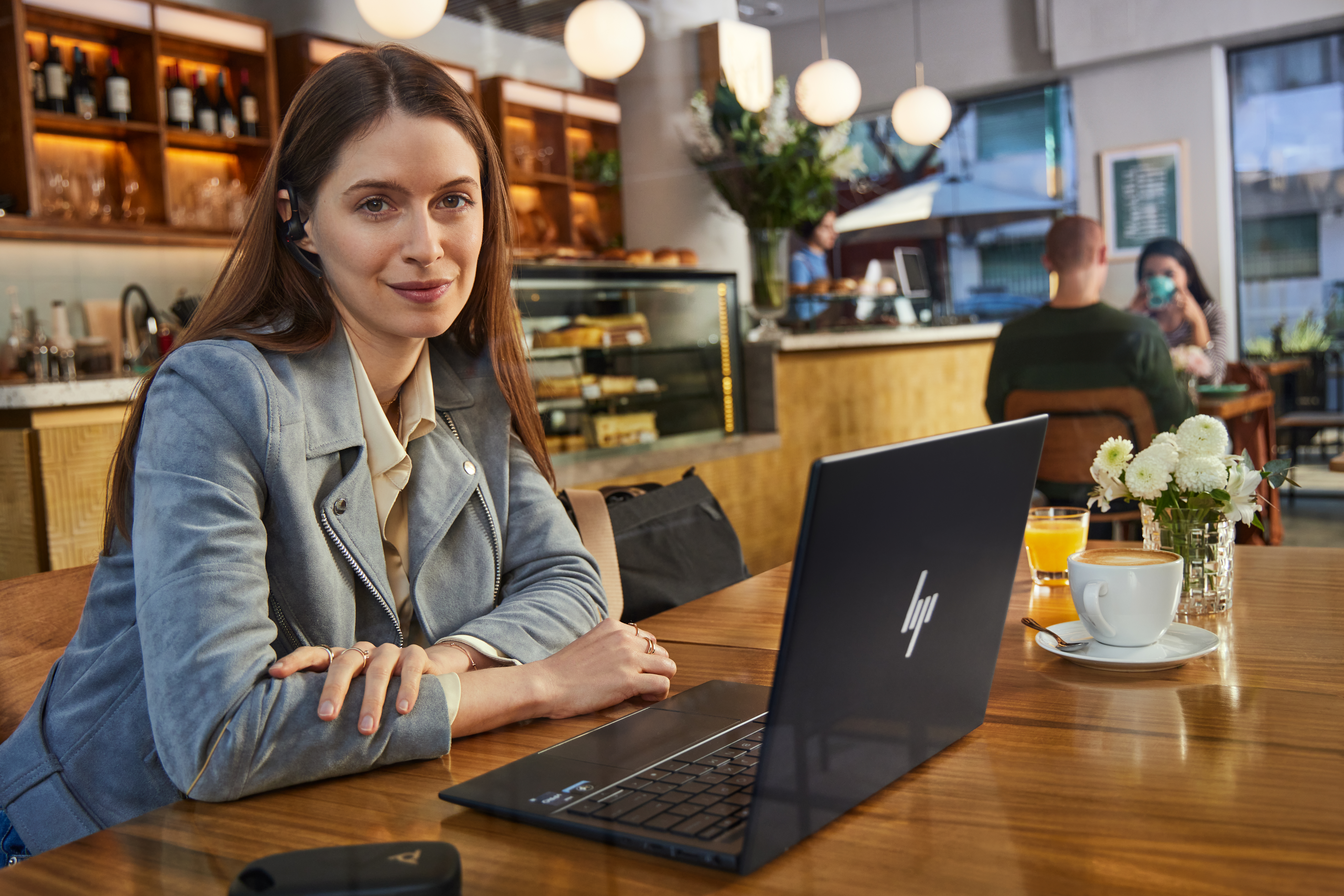 Eine Frau sitzt an einem Holztisch mit einem Laptop, Kaffee und Orangensaft.