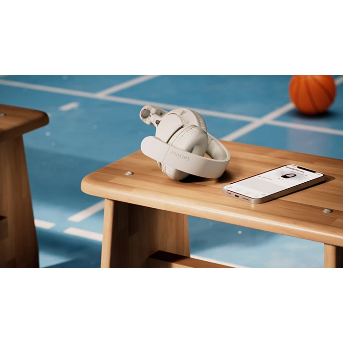 Białe słuchawki Philips spoczywają na drewnianej ławce obok smartfona.