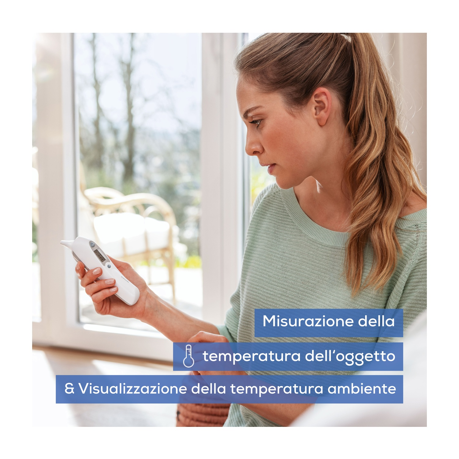 Una donna tiene in mano e guarda un termometro digitale bianco.