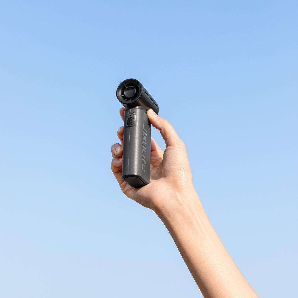 Bir el, mavi gökyüzüne karşı siyah bir vantilatör tutuyor.