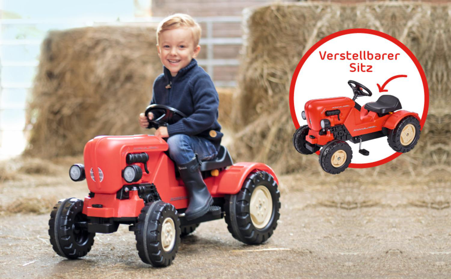 Ein Junge fährt einen roten Spielzeugtraktor in einer Scheune vor Strohballen.