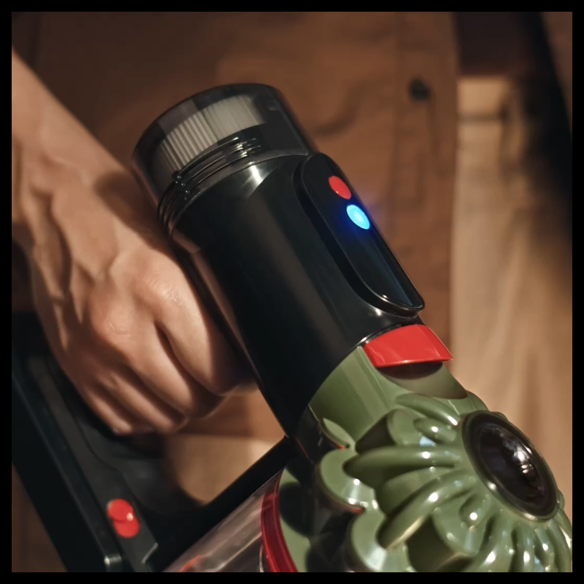 Una mano sostiene una aspiradora negra y verde con luces azules y rojas.