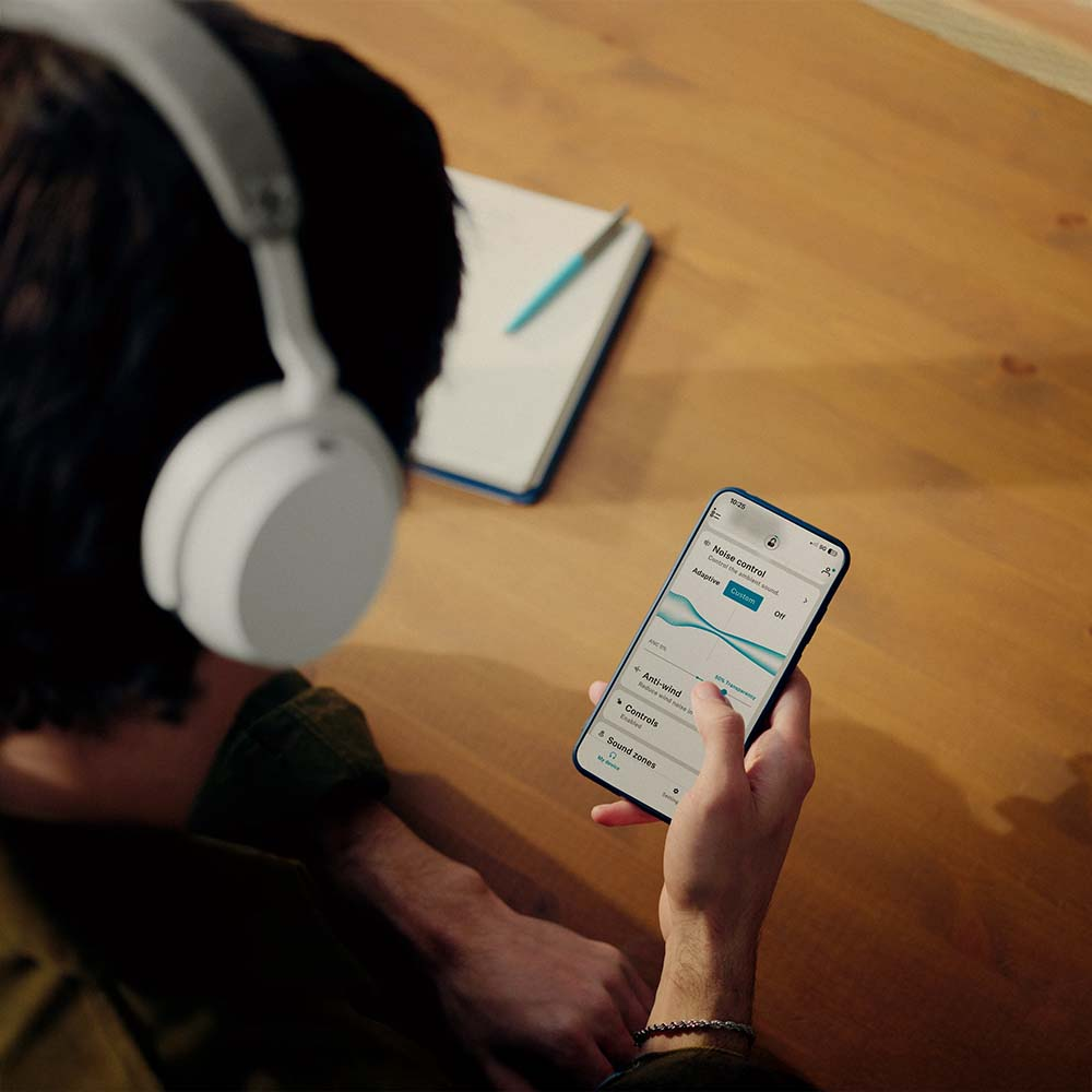 Uomo con cuffie bianche usa app smartphone. Taccuino su tavolo. Scrivania legno.