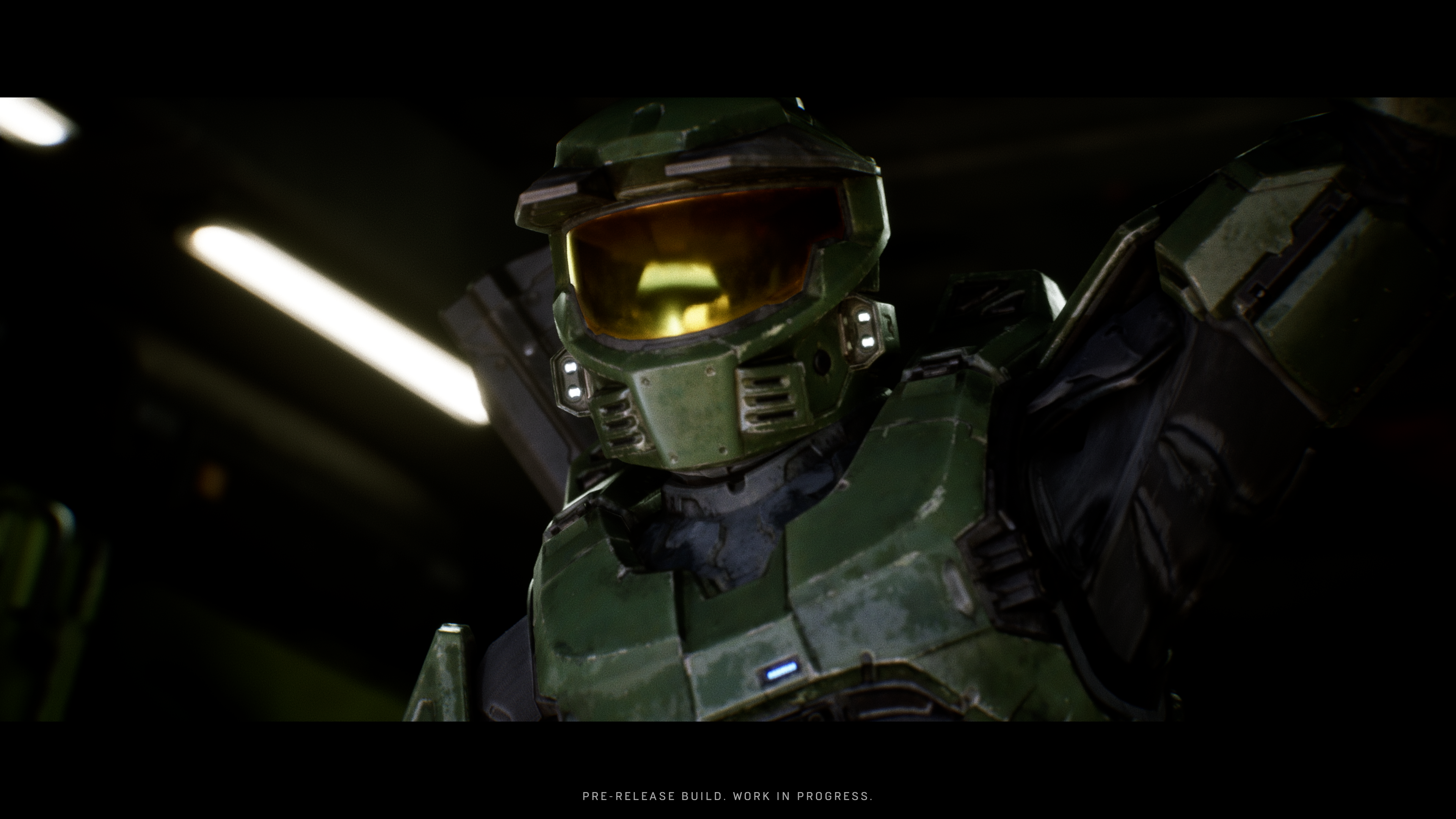 Master Chief en armure verte avec visière dorée, bras levés. Fond sombre.