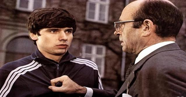 Ein junger Mann mit dunklem Haar und ein älterer Mann mit Brille sprechen.