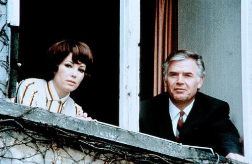 Ein Mann und eine Frau blicken aus einem Fenster. Die Frau trägt ein gestreiftes Oberteil.