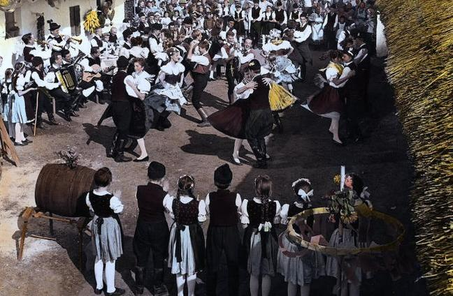 Eine Gruppe von Menschen in Tracht tanzt im Freien, Musik wird gespielt.