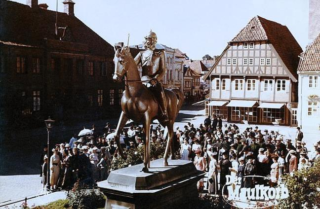 Eine Reiterstatue vor Gebäuden und einer Menschenmenge.