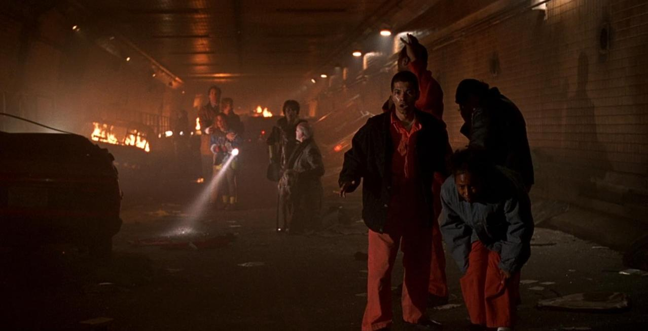Menschen in einem dunklen Tunnel mit Feuer und Rauch im Hintergrund.