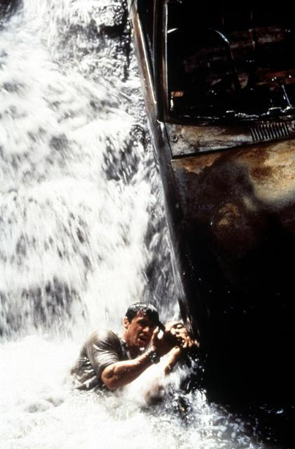Ein Mann kämpft sich durch einen Wasserfall und klammert sich an ein Boot.