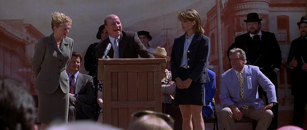 Eine Gruppe von Menschen steht vor einer Kulisse. Ein Mann spricht an einem Podium.