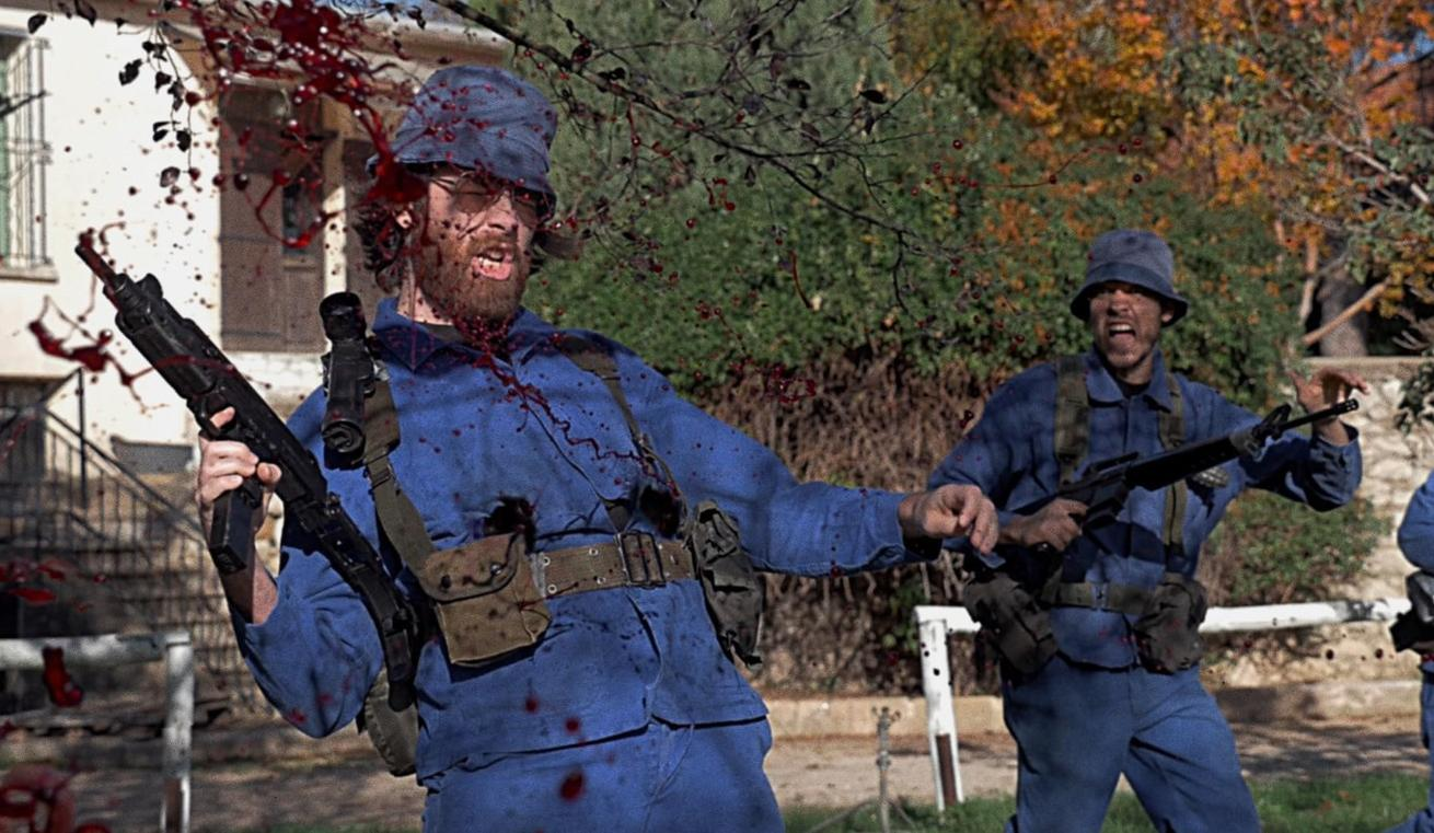 Ein Mann in blauer Uniform wird von Blut getroffen, während er eine Waffe hält.