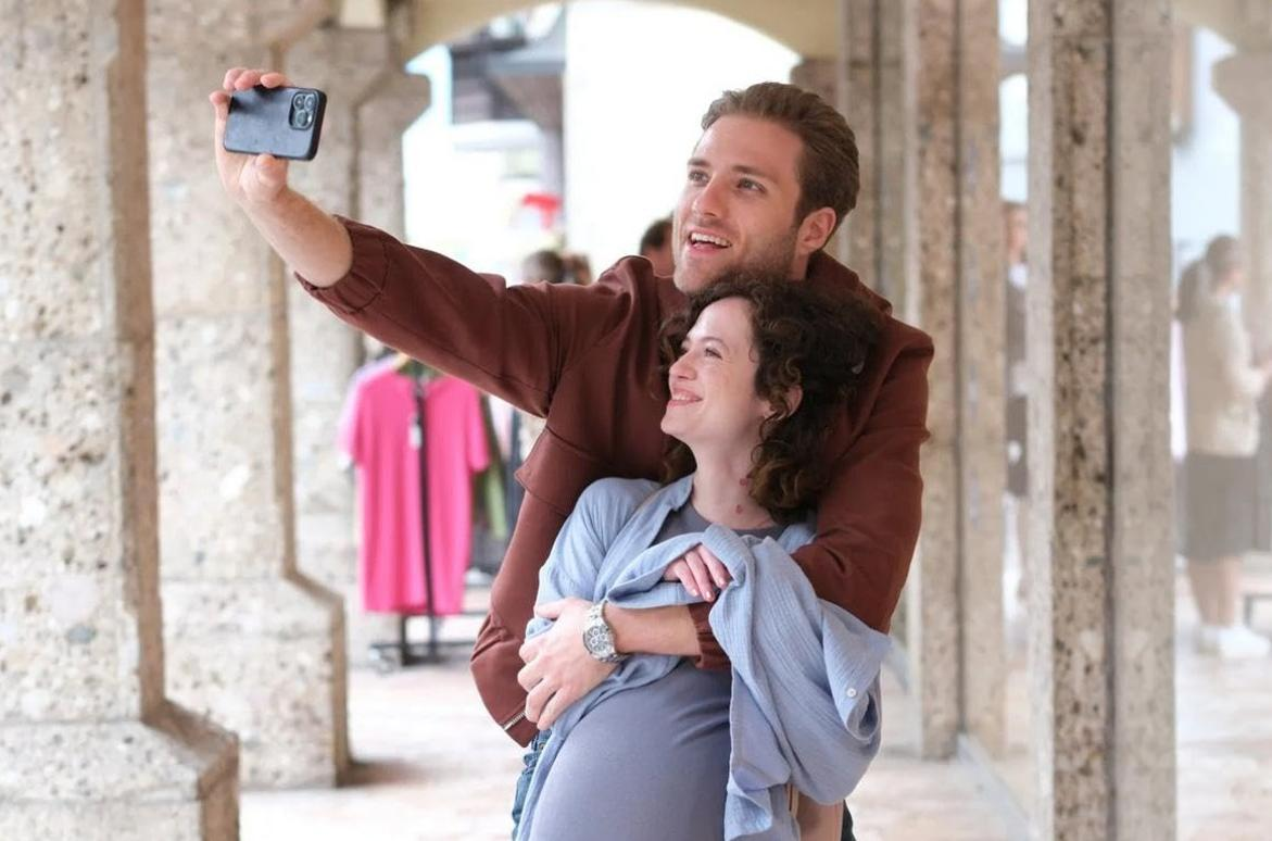 Ein Mann macht ein Selfie mit einer Frau, die er umarmt. Sie stehen draußen.