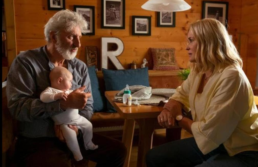 Ein Mann hält ein Baby, eine Frau sitzt gegenüber an einem Holztisch.
