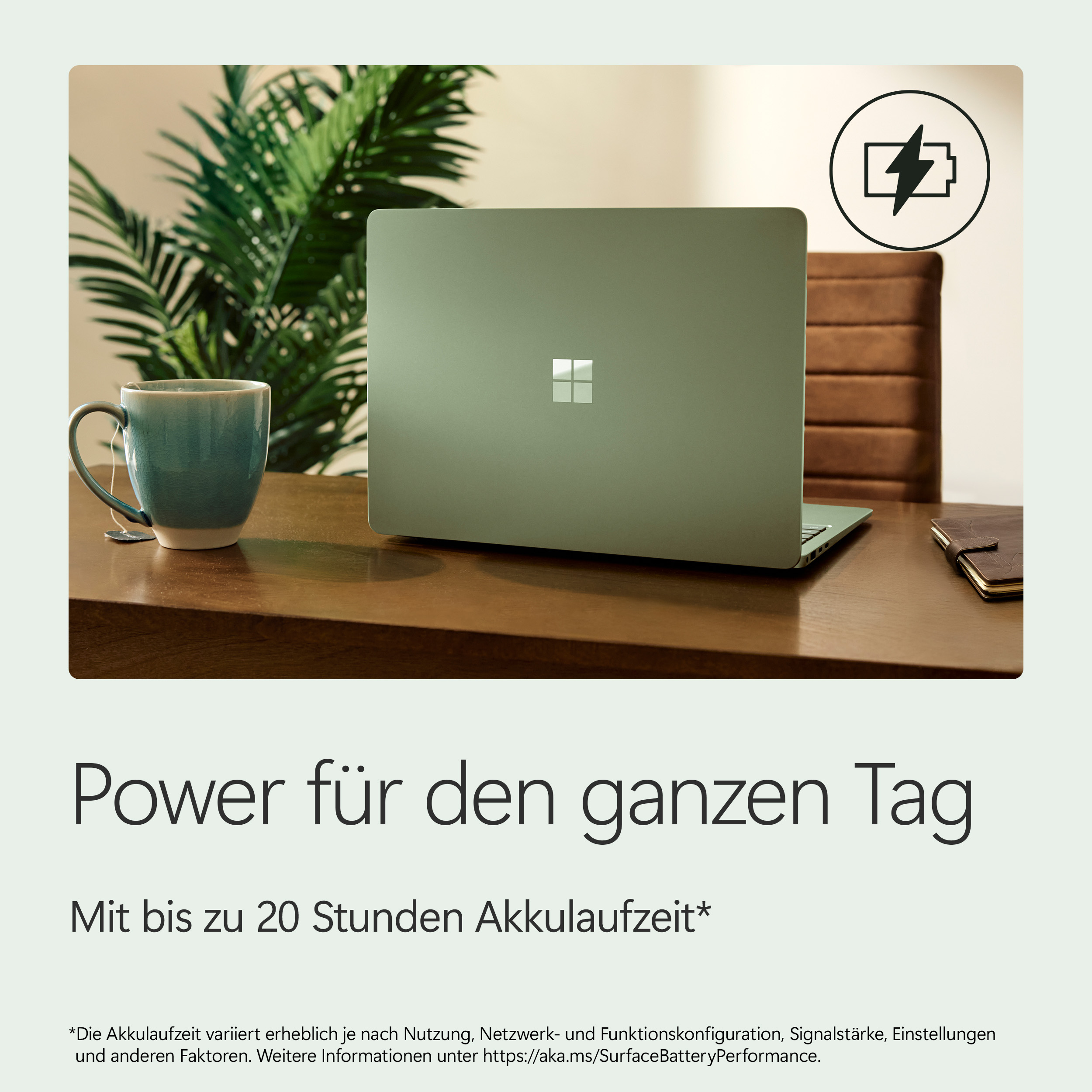 Ein grüner Laptop steht auf einem Holztisch neben einer Tasse und einer Pflanze.
