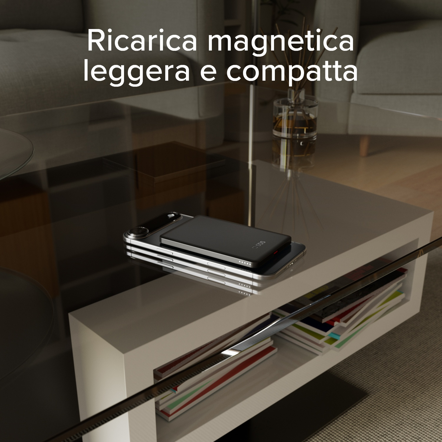 Uno smartphone nero si ricarica su un tavolo bianco, riviste accanto.