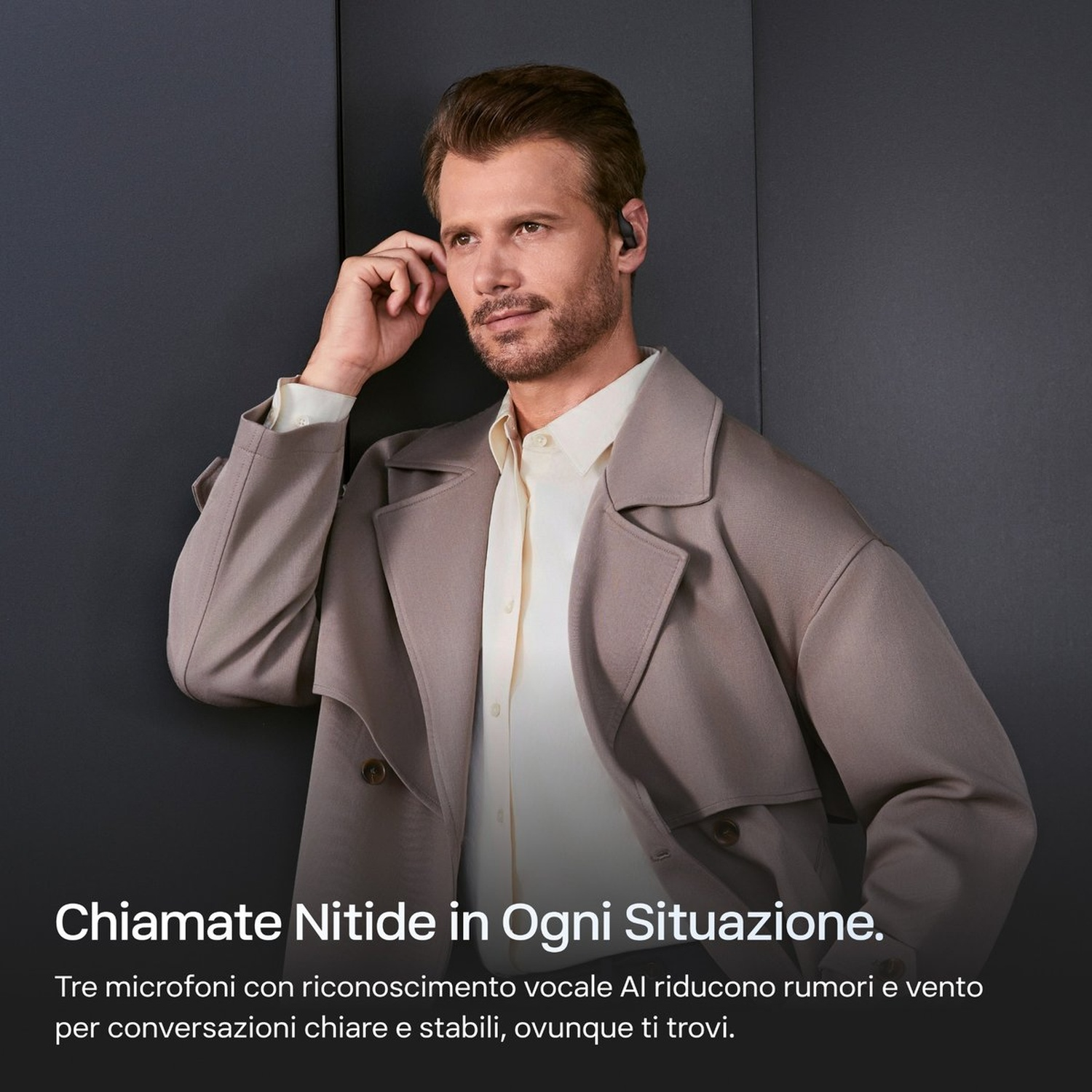 Un uomo con auricolari, cappotto e camicia davanti a uno sfondo scuro.