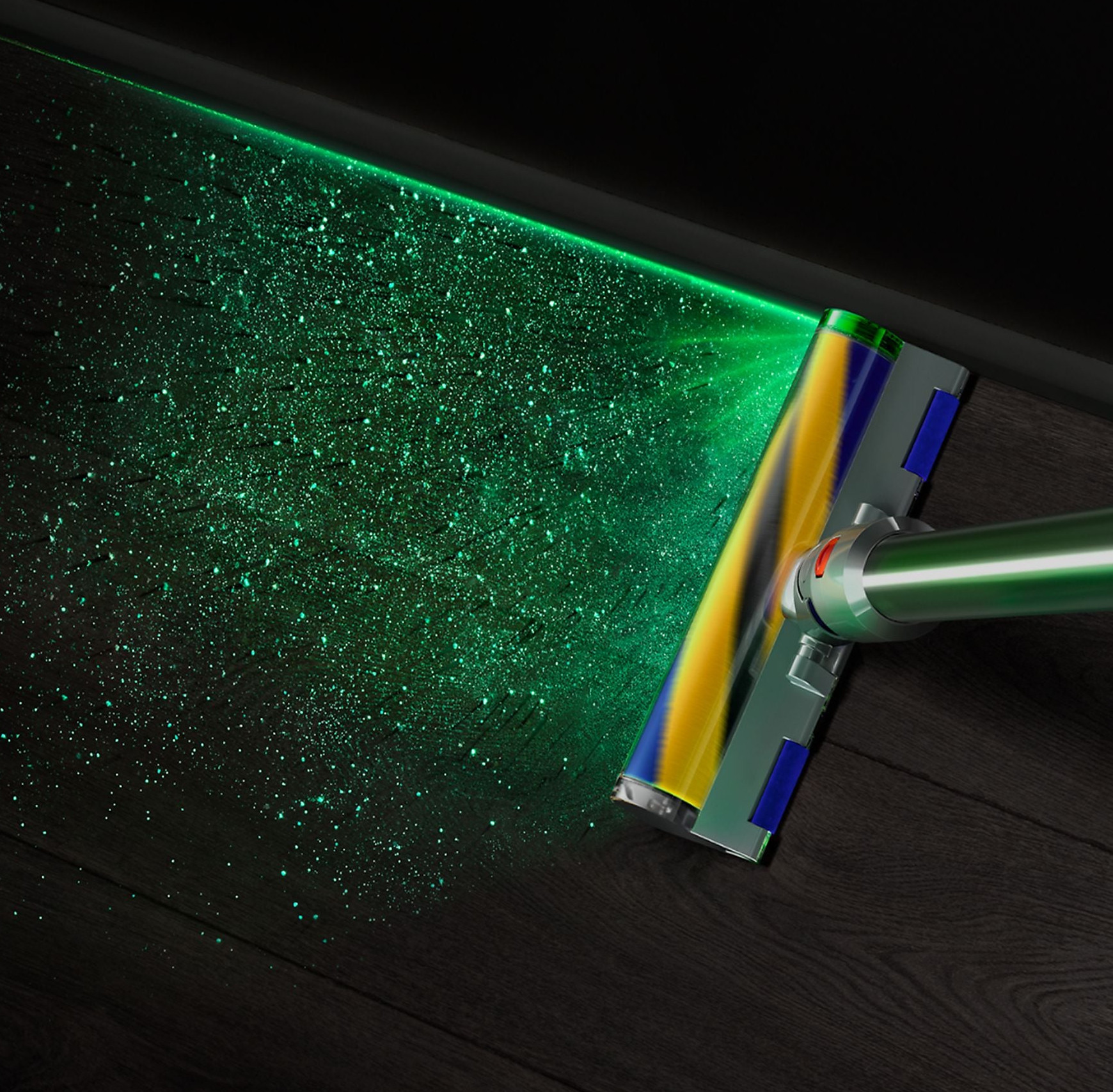 Głowica odkurzacza z zielonym światłem laserowym oświetla cząsteczki kurzu na ciemnej drewnianej podłodze.