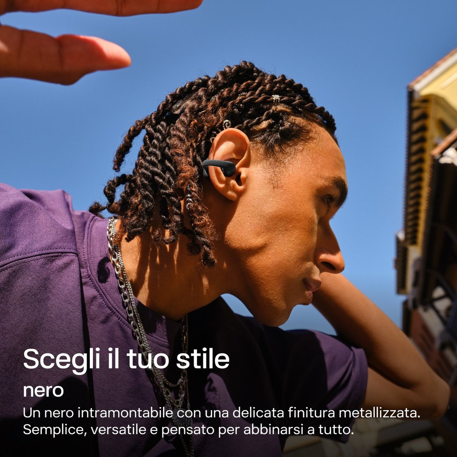 Uomo con capelli intrecciati indossa auricolari e maglia viola.
