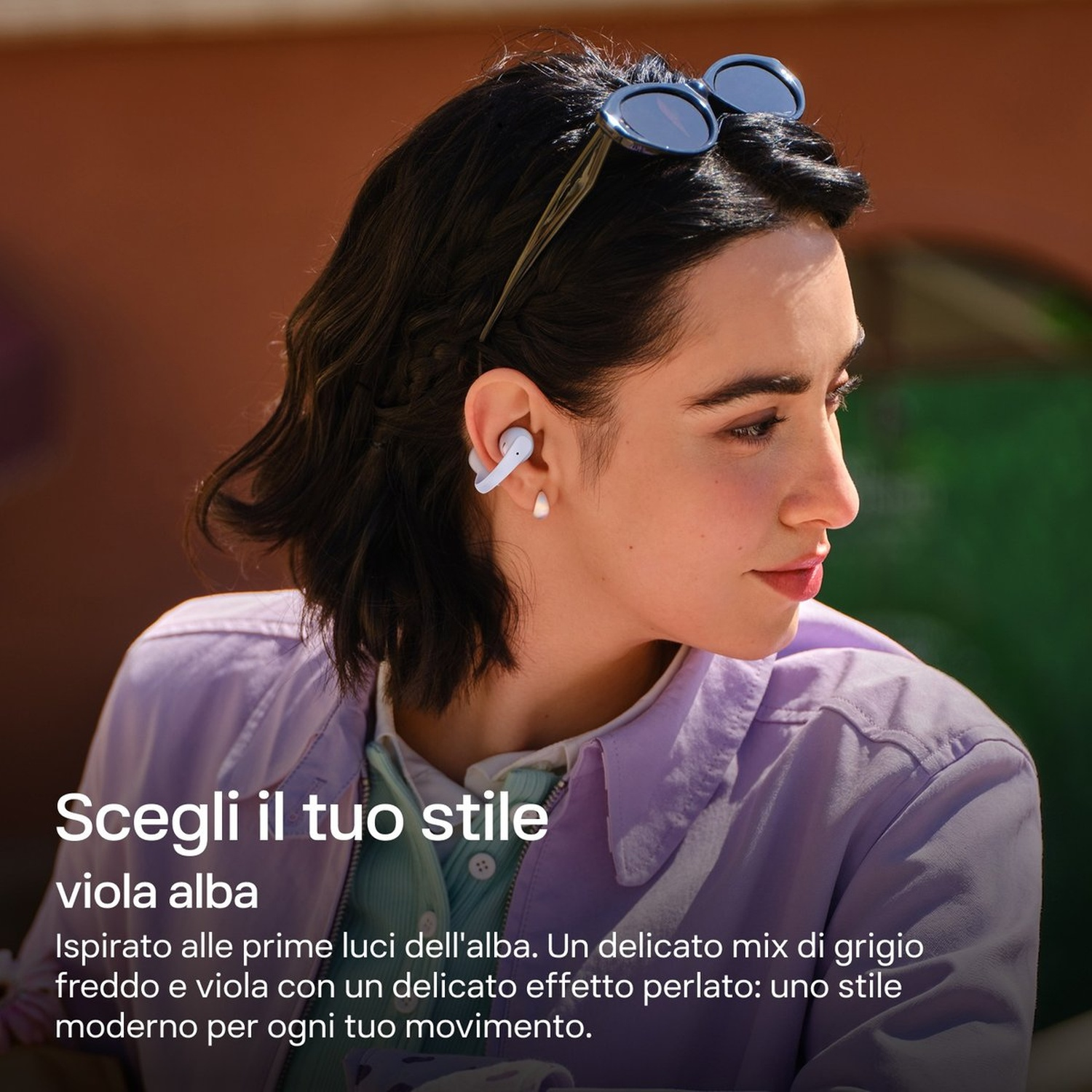 Donna con auricolari, occhiali da sole in testa, giacca lavanda.