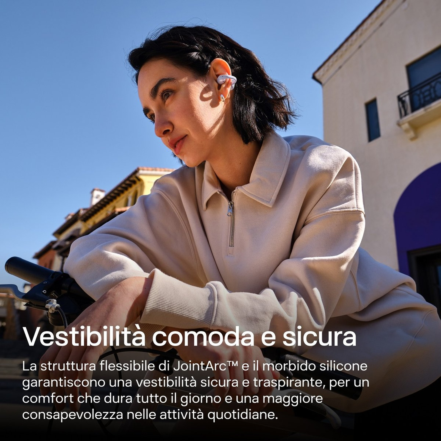 Una donna con auricolari appoggiata a una bicicletta davanti a edifici.