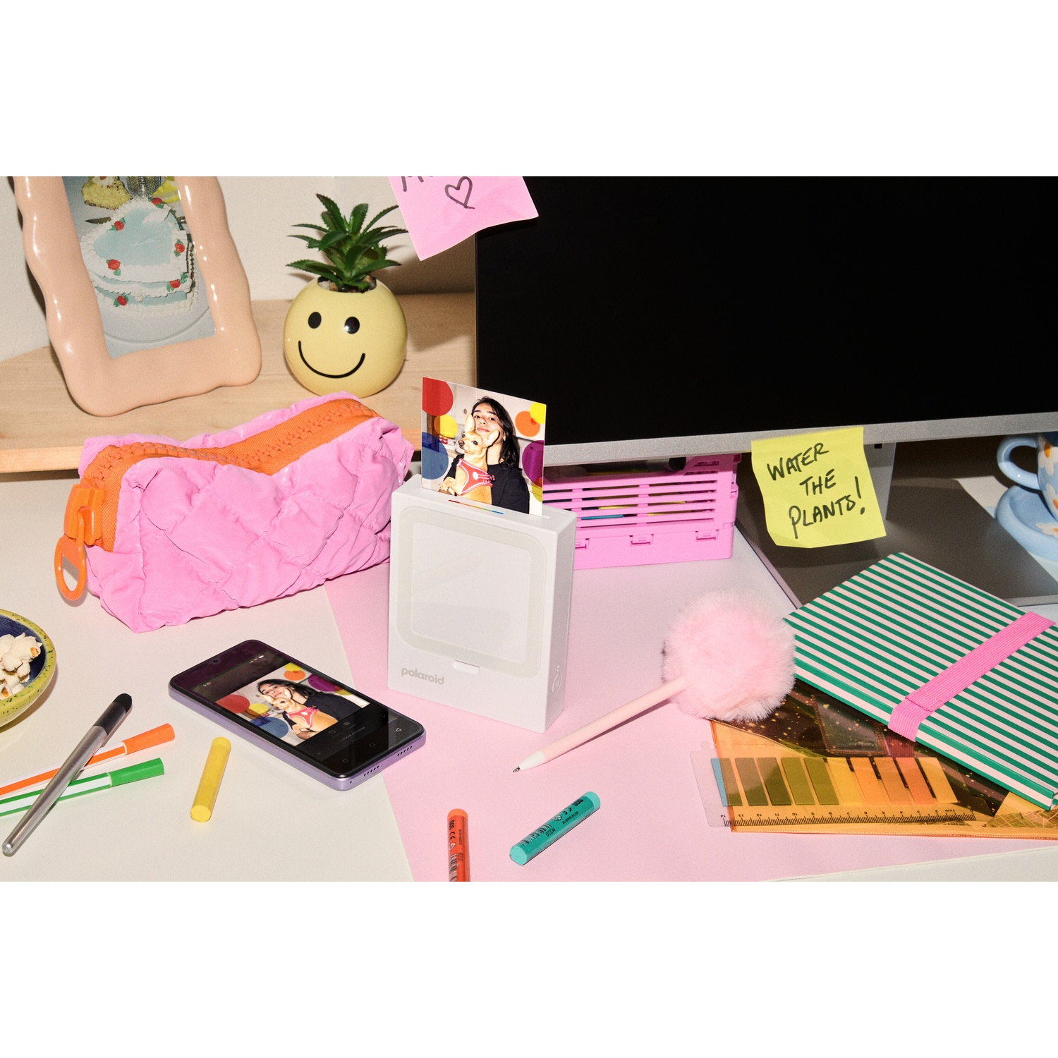 Un bureau avec une imprimante Polaroid, un téléphone, des stylos et des carnets.