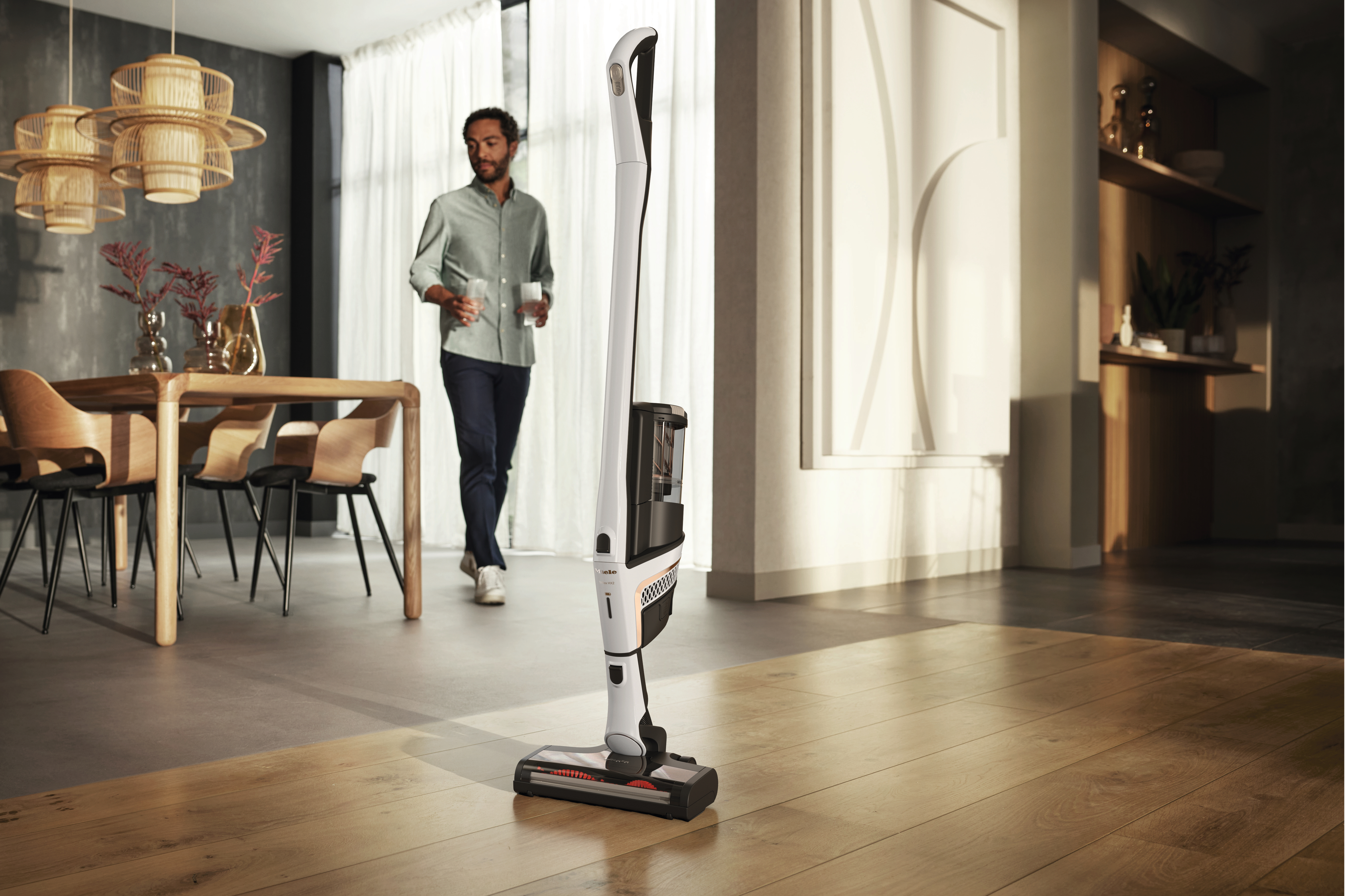 Ein Mann geht durch ein modernes Esszimmer, ein kabelloser Staubsauger steht im Vordergrund.