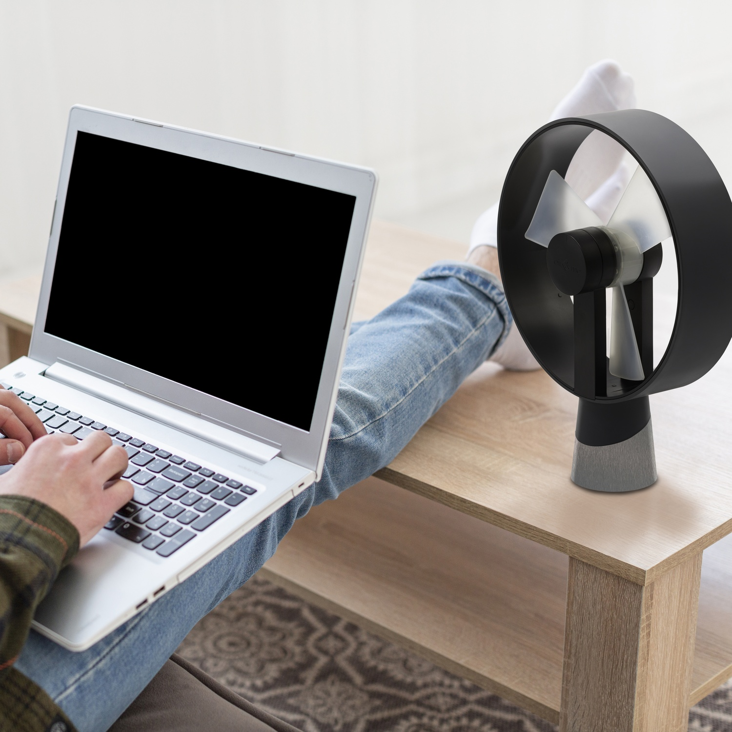Persoon typt op laptop, kleine zwarte ventilator ernaast.