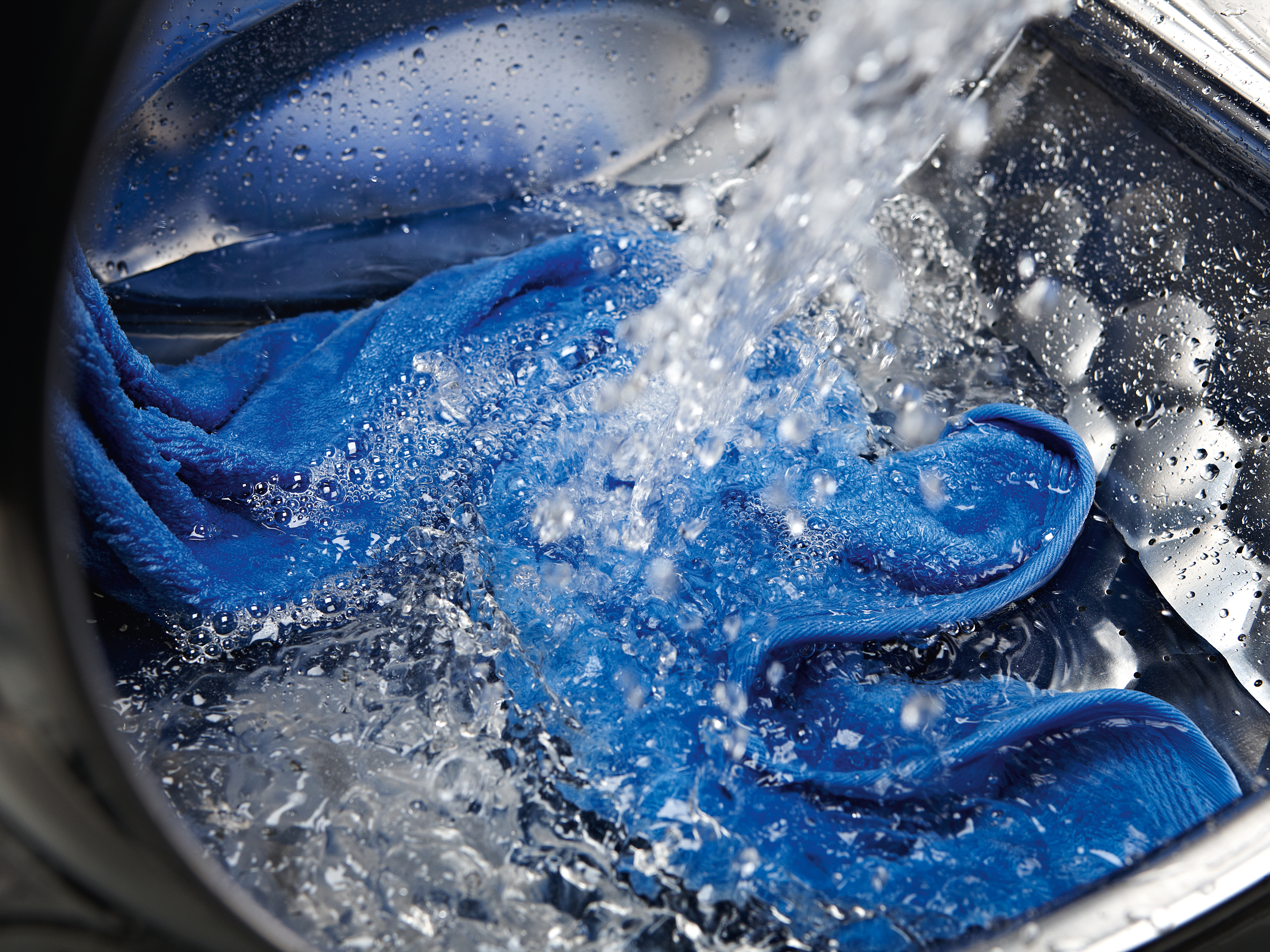 Ein blaues Tuch wird in einer Waschmaschine mit Wasser übergossen.