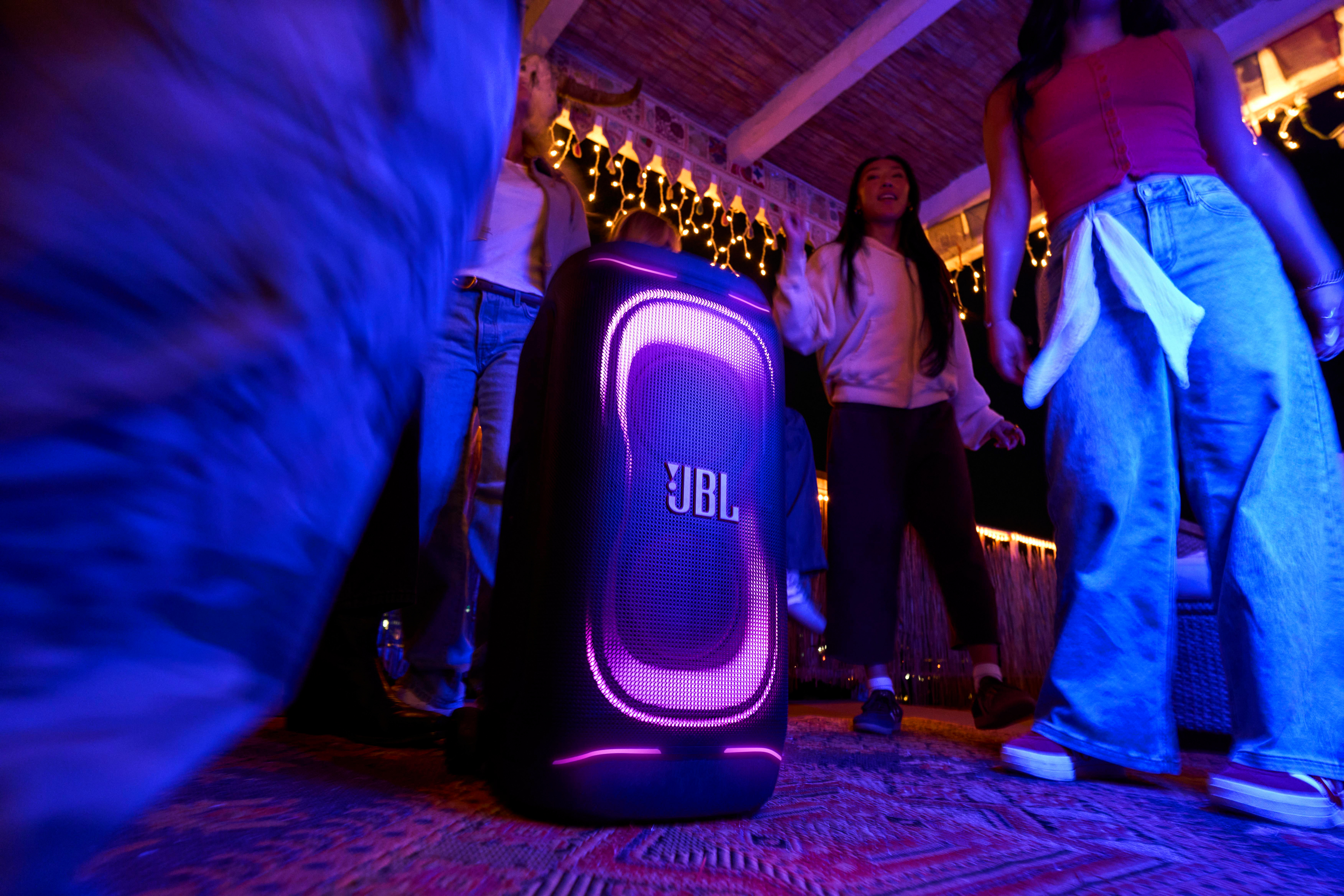 Leute tanzen zu einem JBL-Lautsprecher mit lila Lichtern in einer dunklen Nacht.