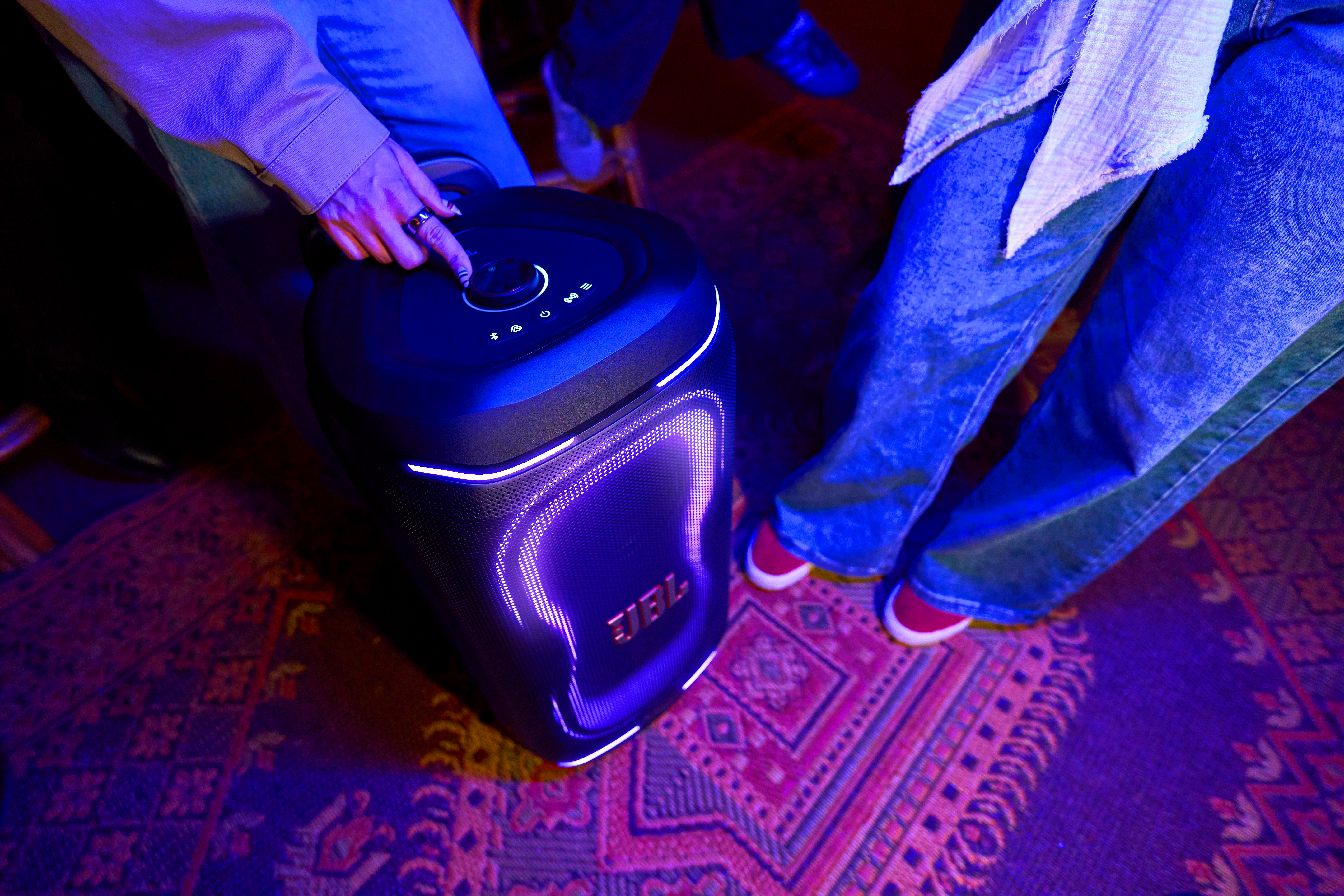 Eine Person bedient einen JBL-Lautsprecher mit lila Lichtern auf einem Teppich.