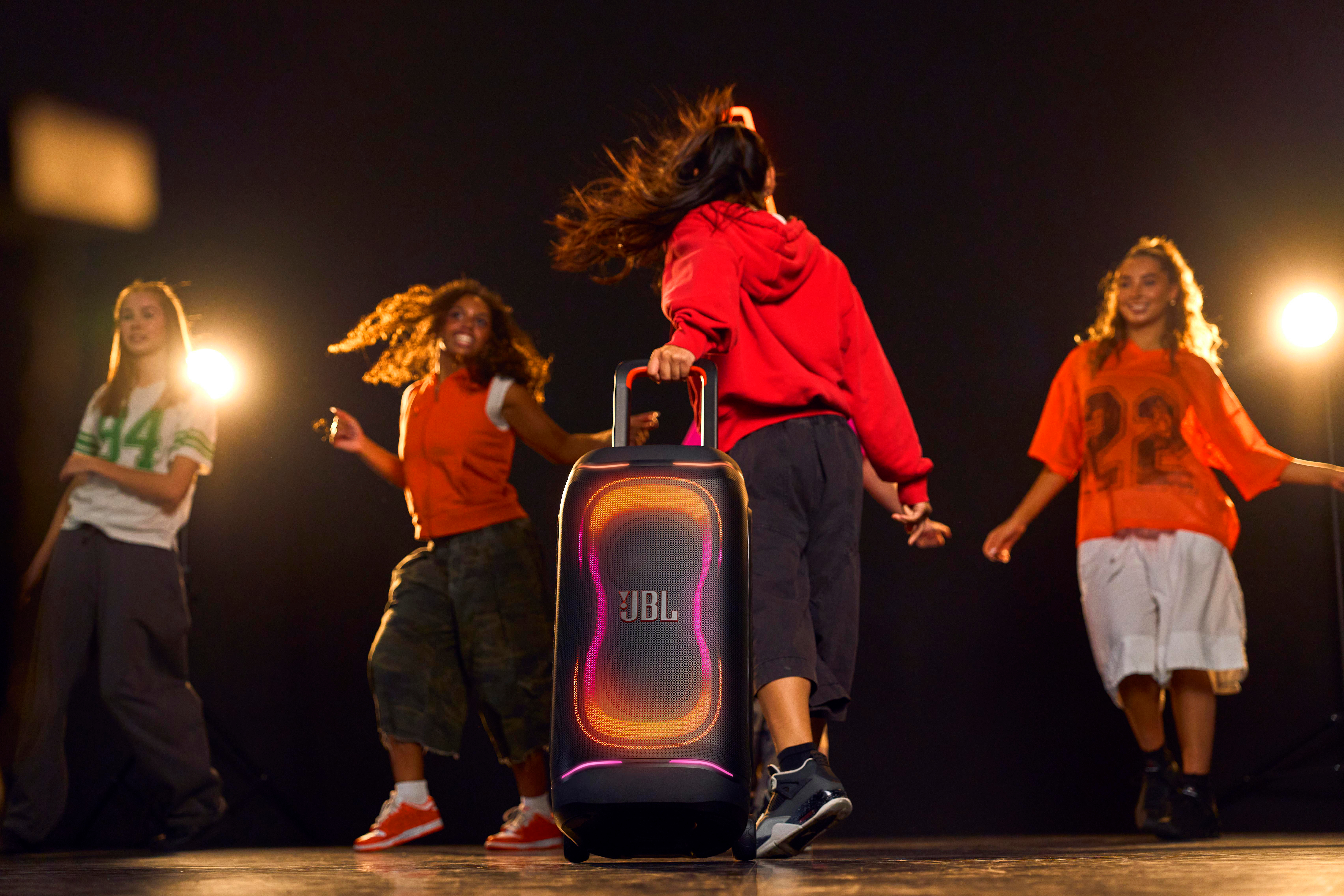Vier Tänzer bewegen sich um eine JBL-Box mit bunten Lichtern.