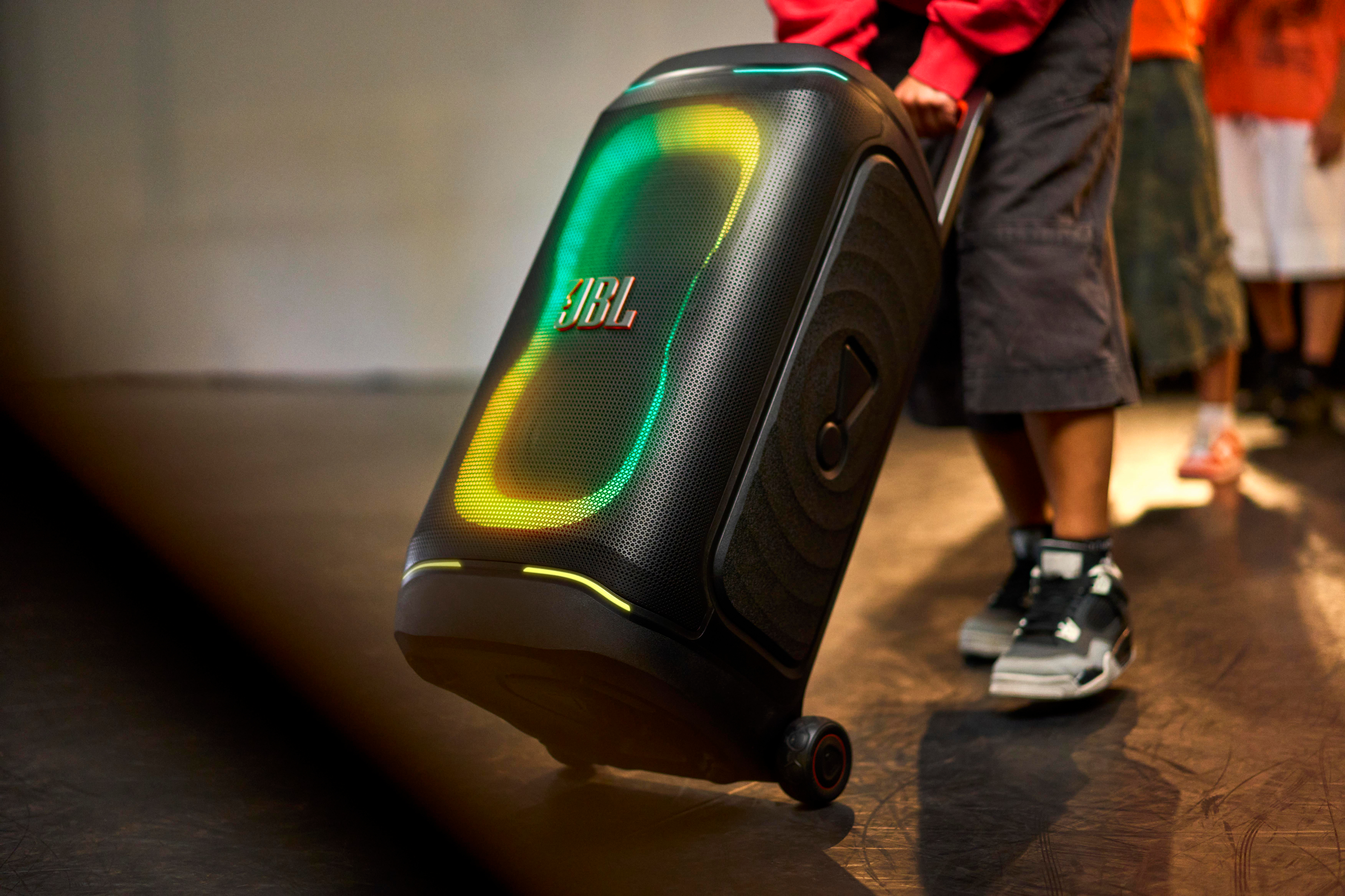 Schwarzer Trolley mit JBL-Logo und bunten Lichtern, von einer Person gezogen.