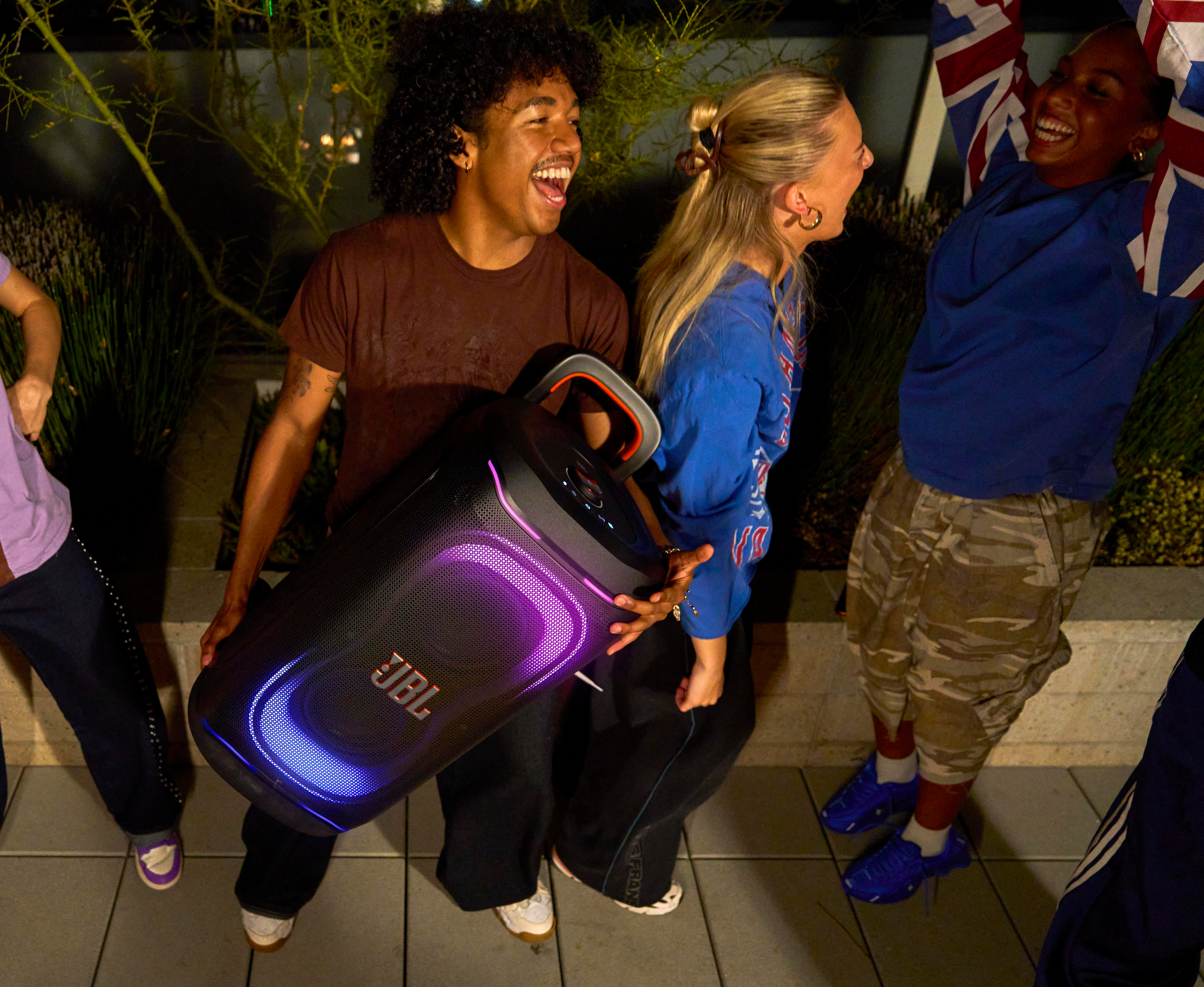 Leute feiern mit einer JBL-Box bei Nacht, eine Person hält eine britische Flagge.