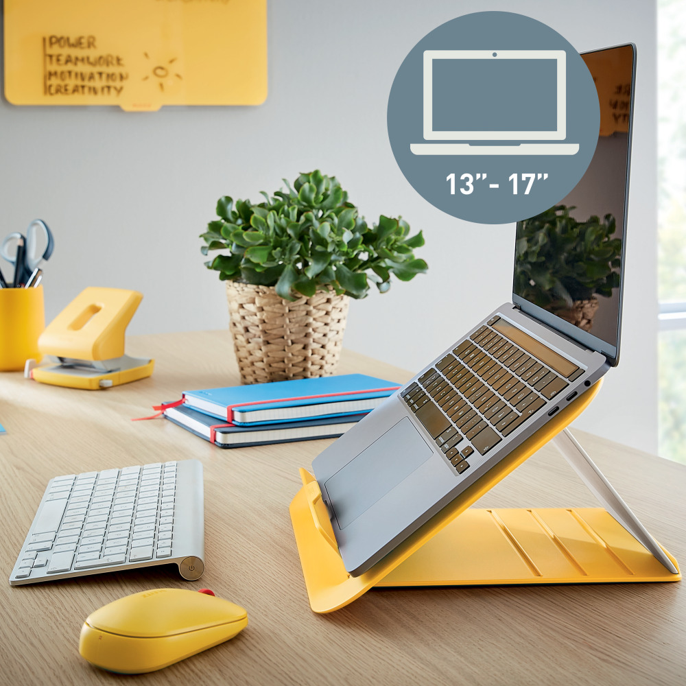 Laptop sárga állványon, faasztalon. Billentyűzet, egér, jegyzetfüzetek, növény látható.