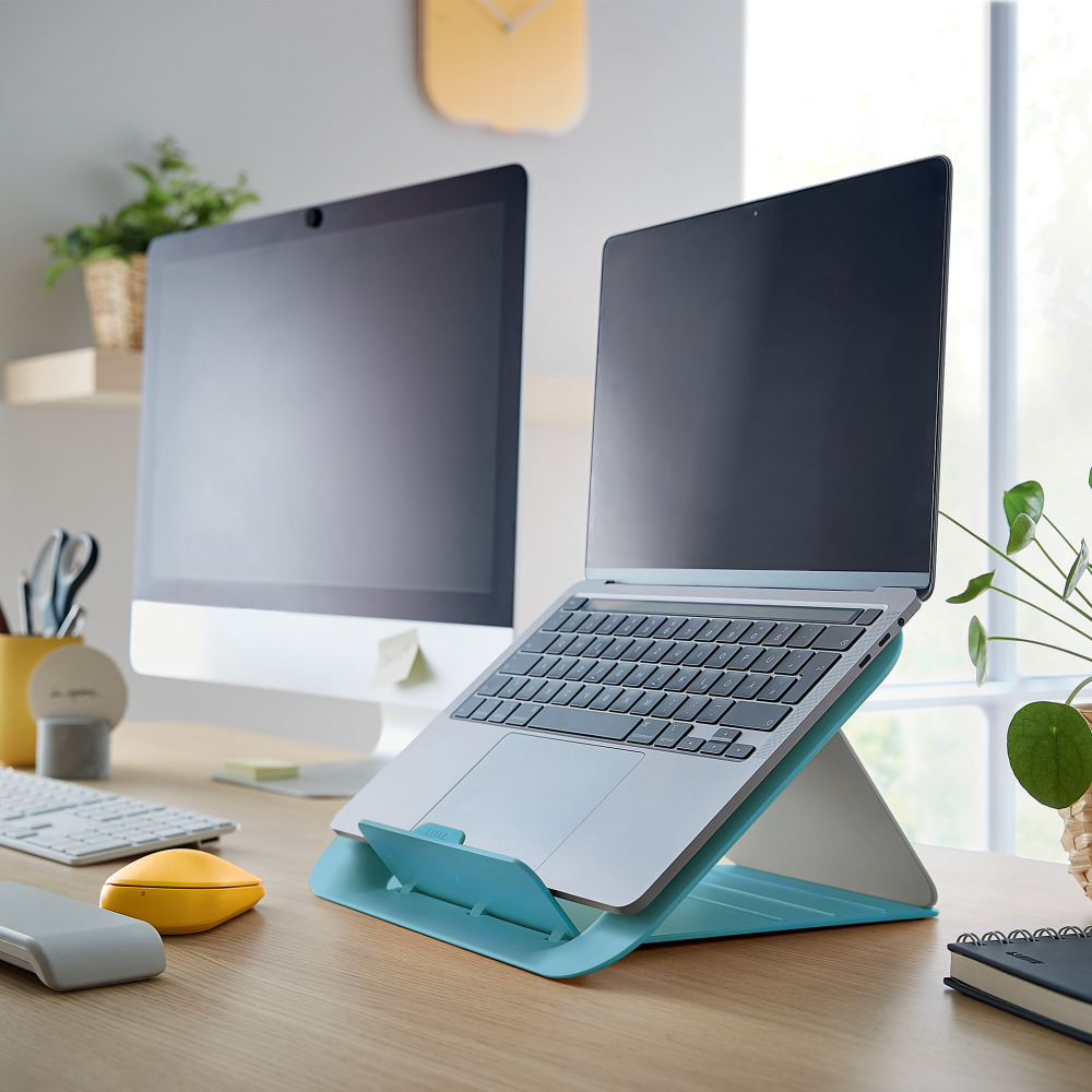 Egy laptop kék állványon monitor mellett egy asztalon.