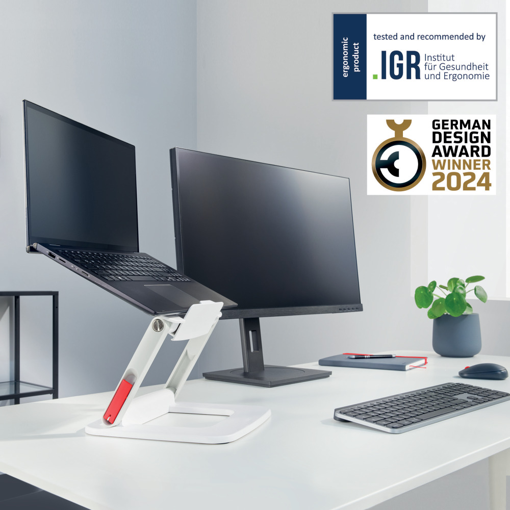 Laptop és monitor ergonomikus állványon az asztalon. Díjak láthatók.