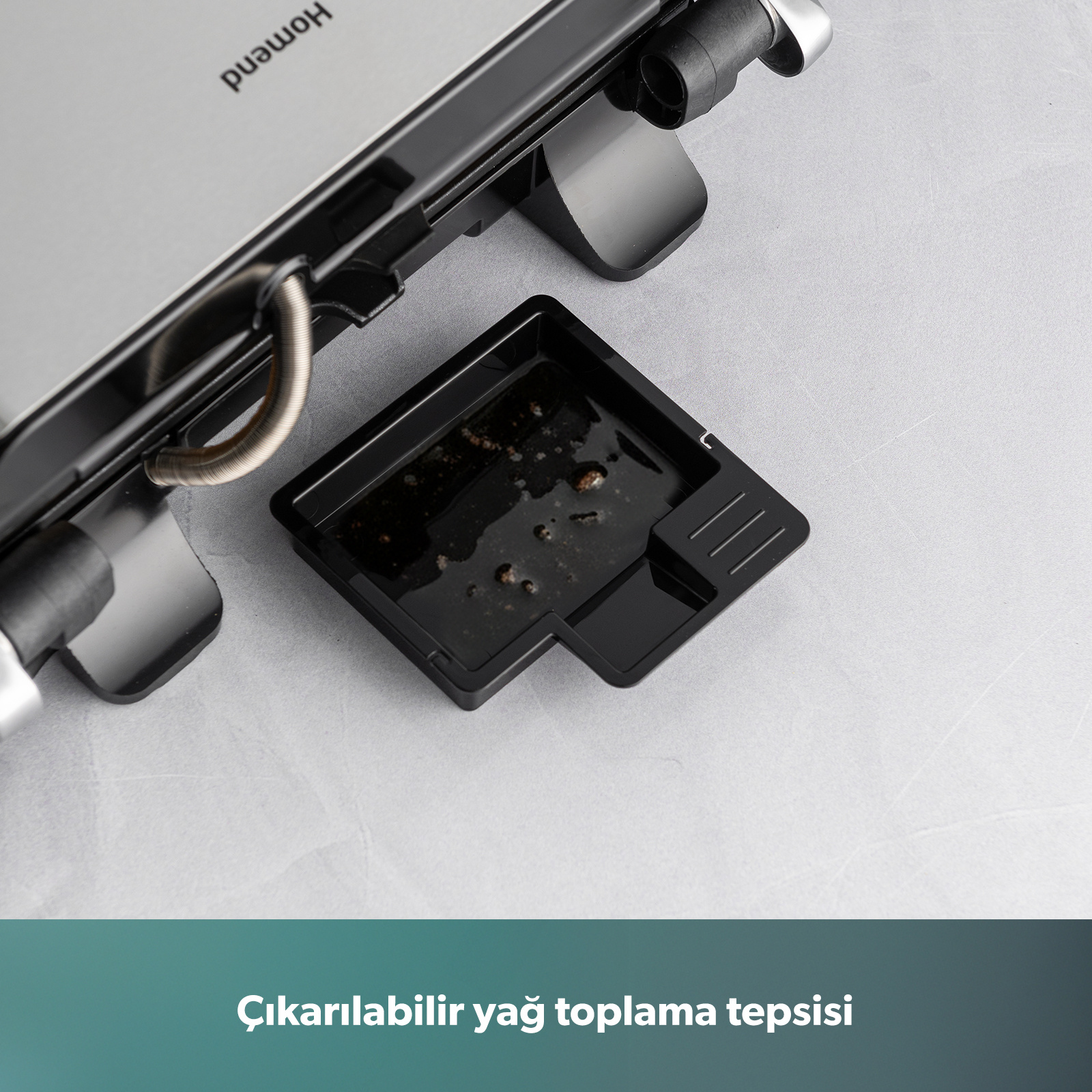 Kahverengi kalıntılı siyah damlama tepsisi, açık bir tost makinesinin yanında.