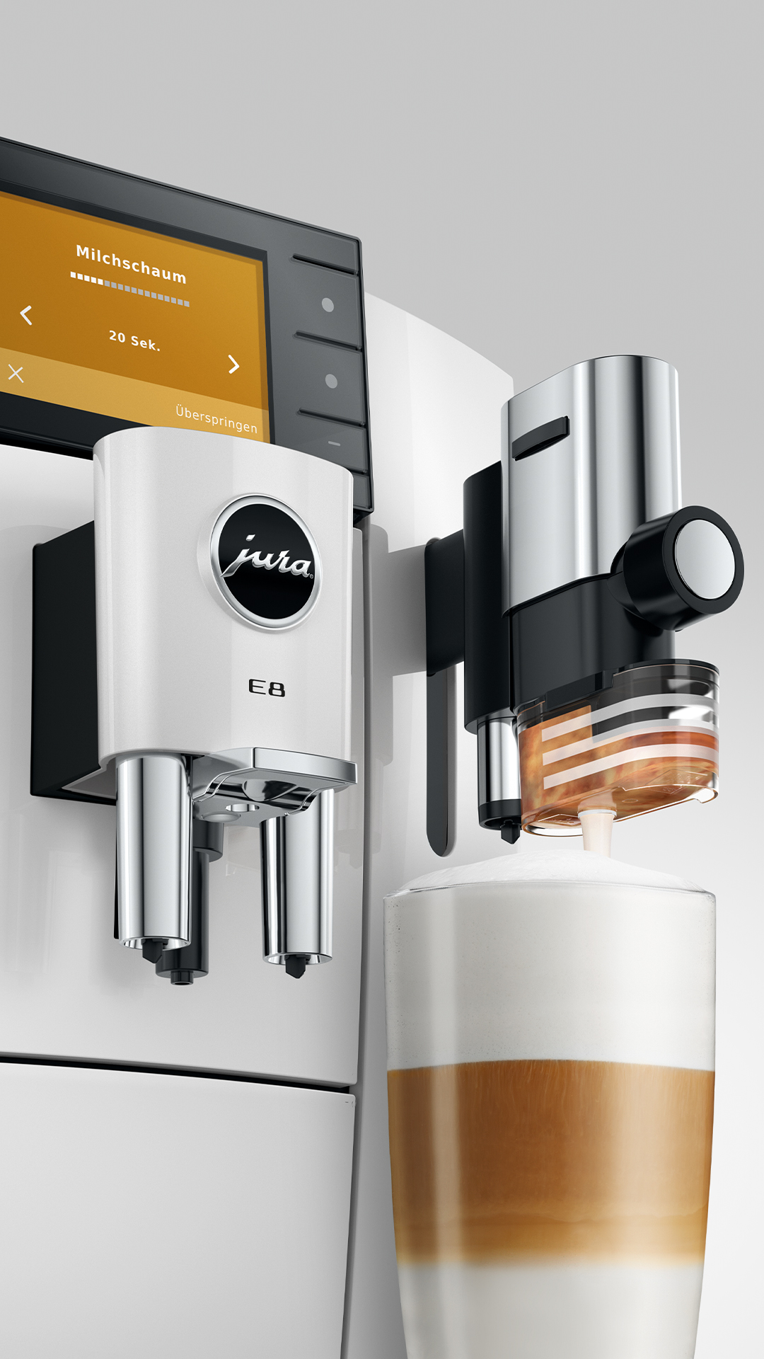 Egy króm részletekkel ellátott fehér kávéfőző latte macchiato-t készít.