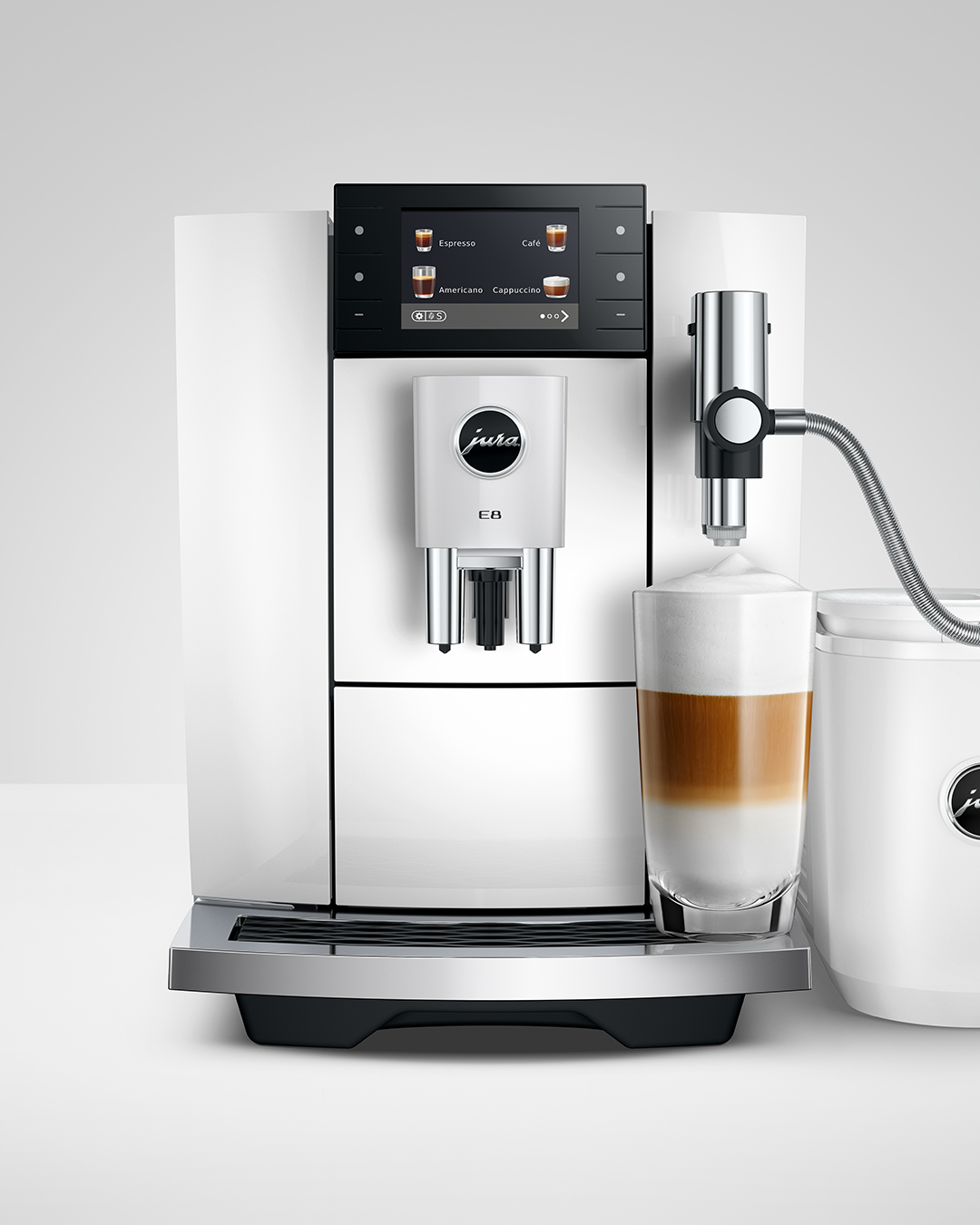 Egy fehér kávéfőző latte macchiato pohárral és tejtartóval.