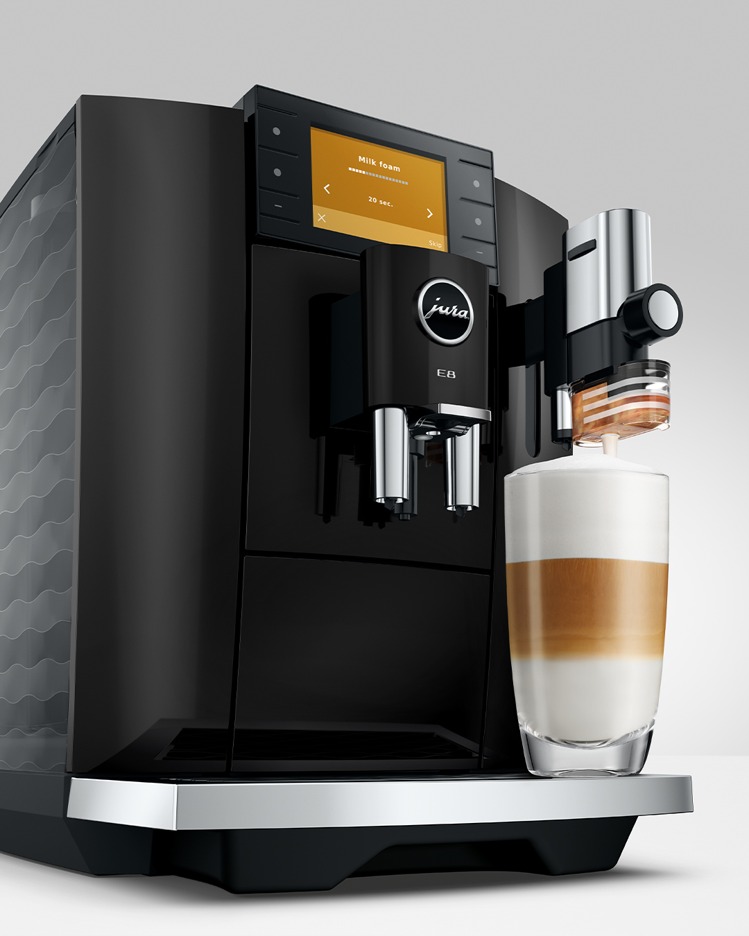 Egy fekete kávéfőző latte macchiato-t készít egy pohárba.