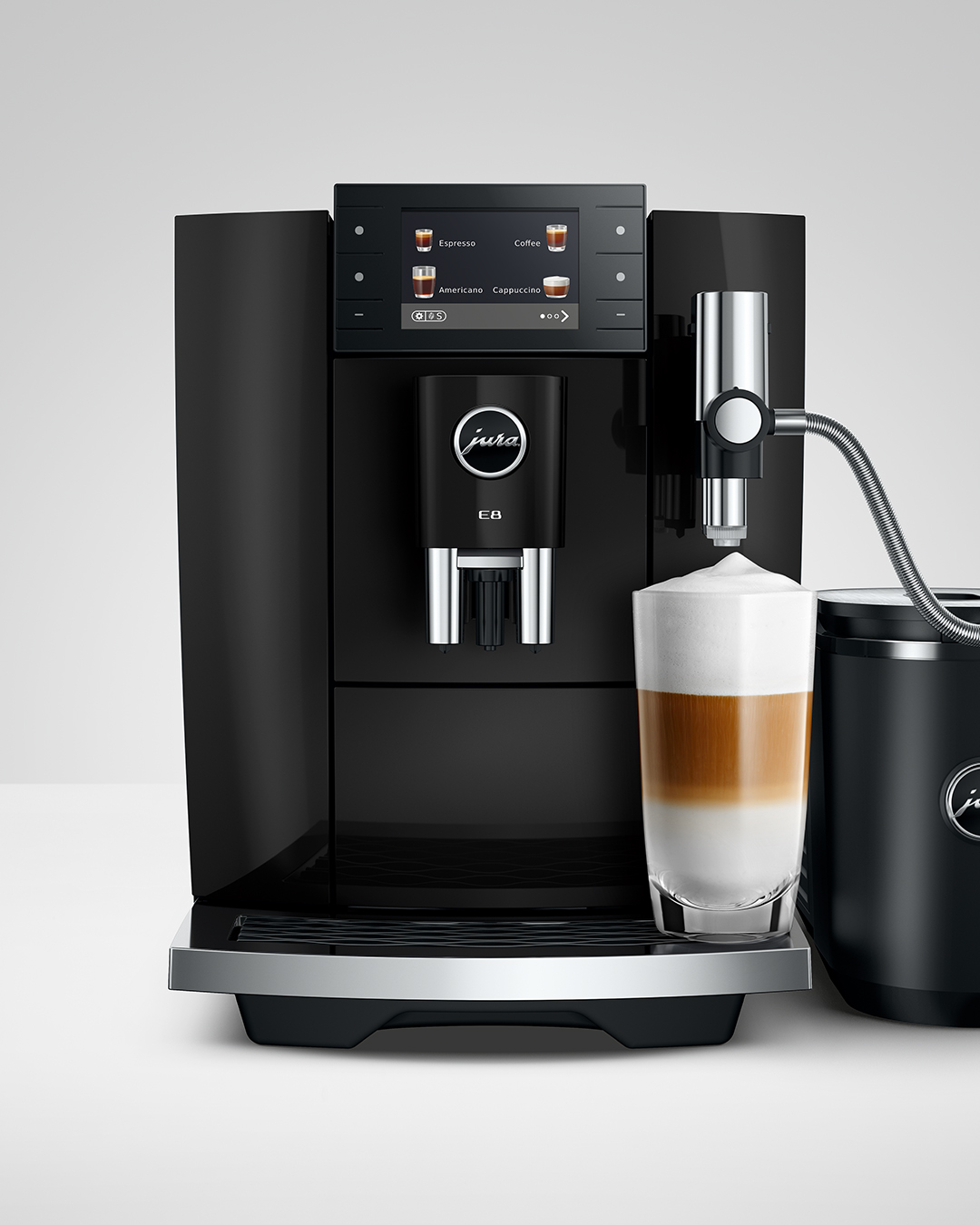 Egy modern fekete Jura E8 kávéfőző réteges lattét készít egy pohárban.