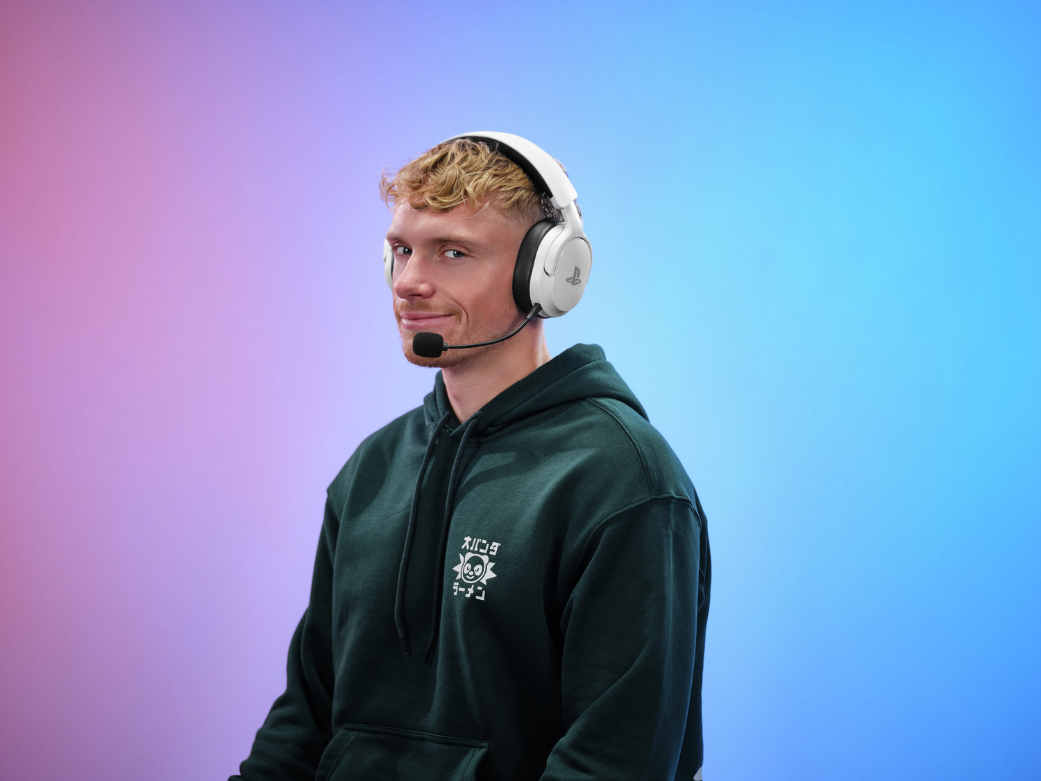Un hombre de pelo rubio lleva auriculares blancos y una sudadera verde oscuro.